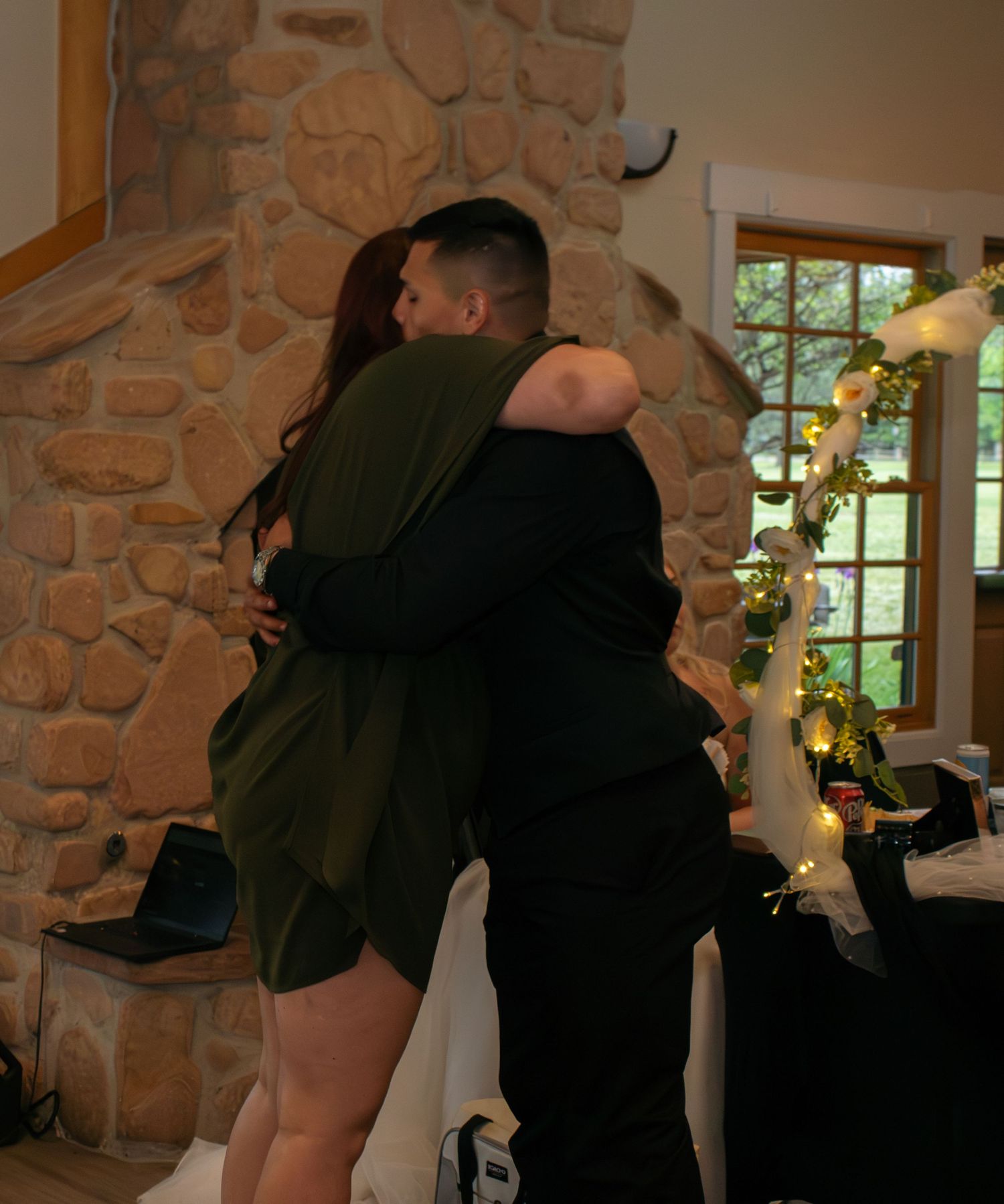 Emotional wedding embrace captured during reception by stone fireplace.