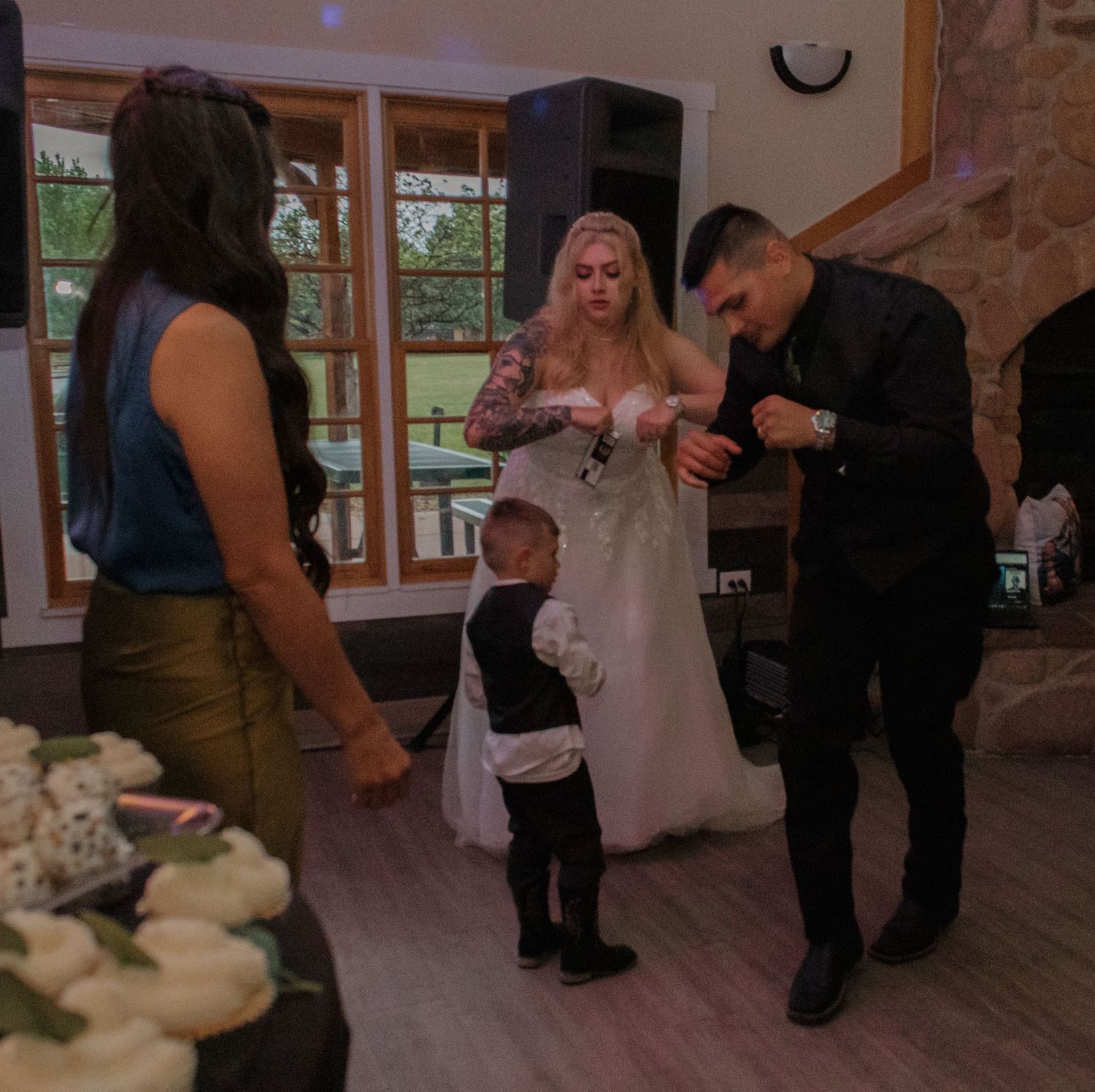 Wedding guests interacting during a reception in a room with stone walls and large windows.