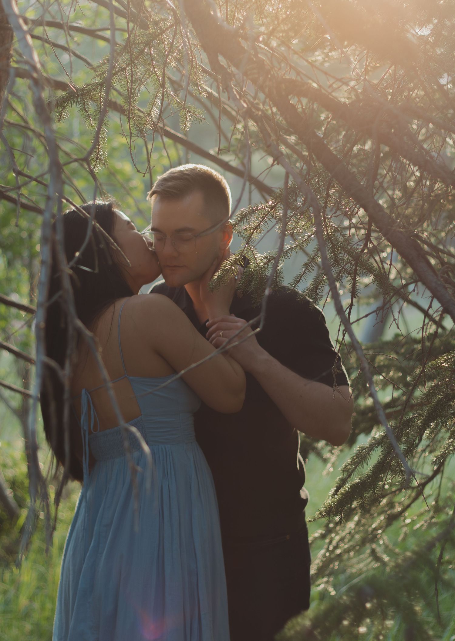 Romantic couple embracing in a sunlit forest with golden light filtering through branches.