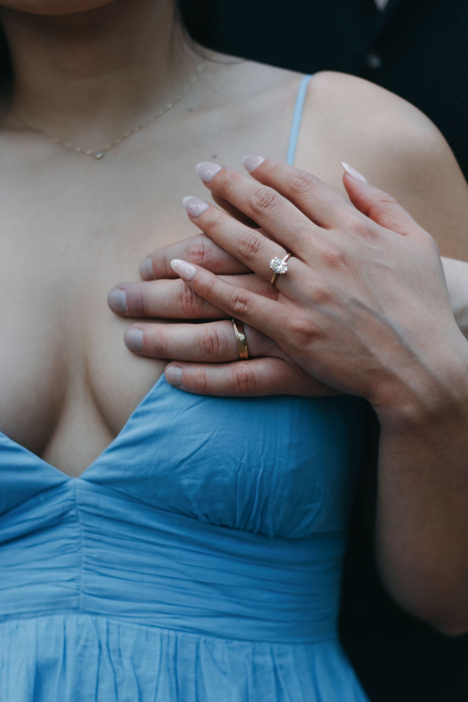 Detailed shot of hands with diamond ring resting on a blue dress.