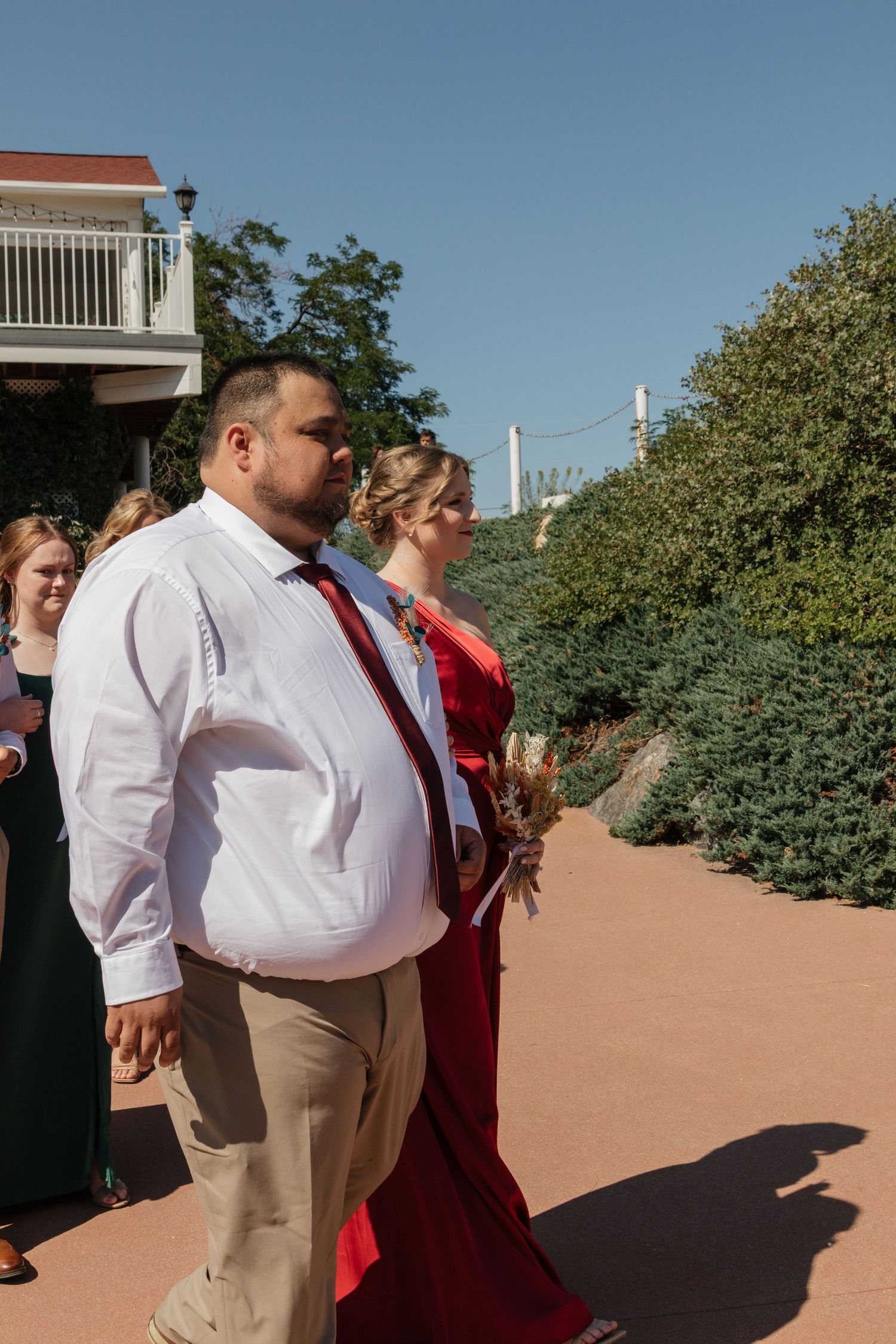 Wedding party members in formal attire gather outdoors on a sunny patio.