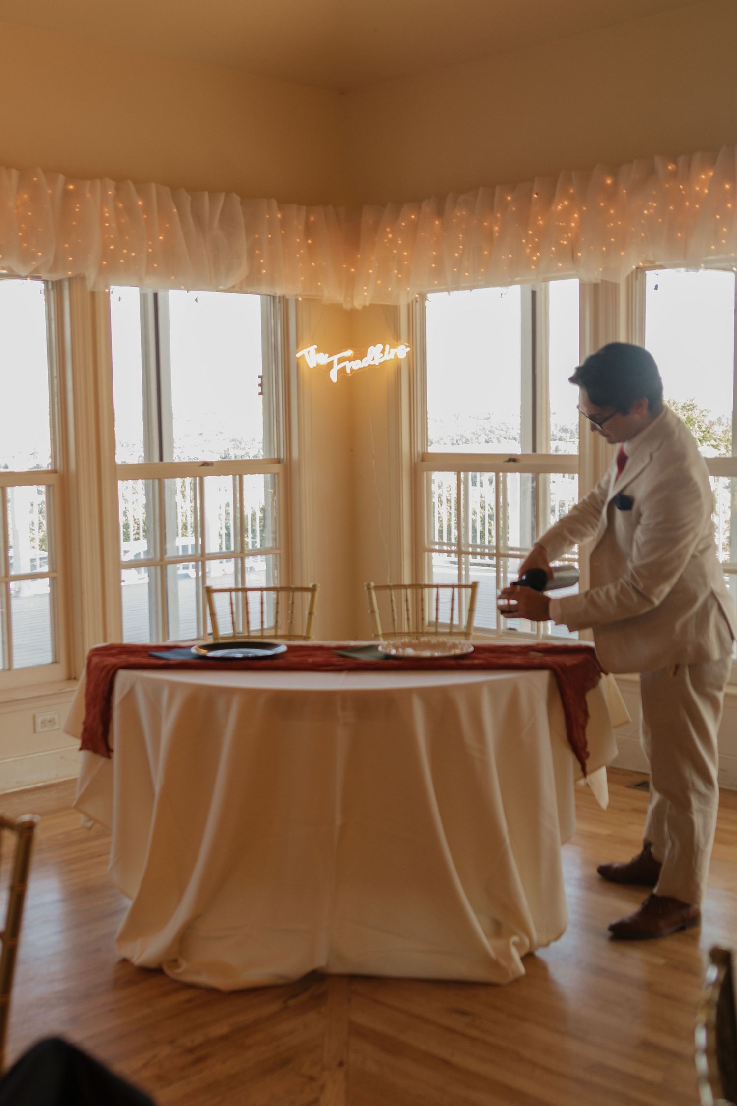 Wedding reception setup with fairy lights and white tablecloth in a sunlit room.