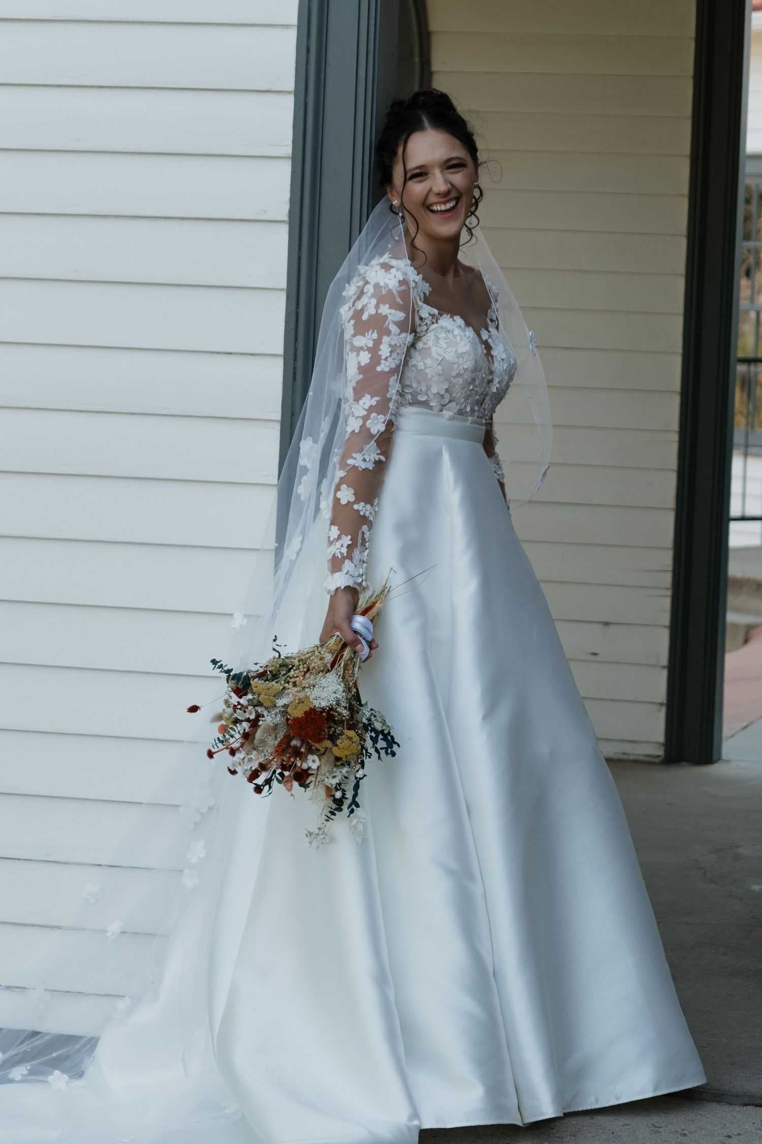 A stunning bridal portrait showcasing a lace-sleeved wedding gown and dried flower bouquet.