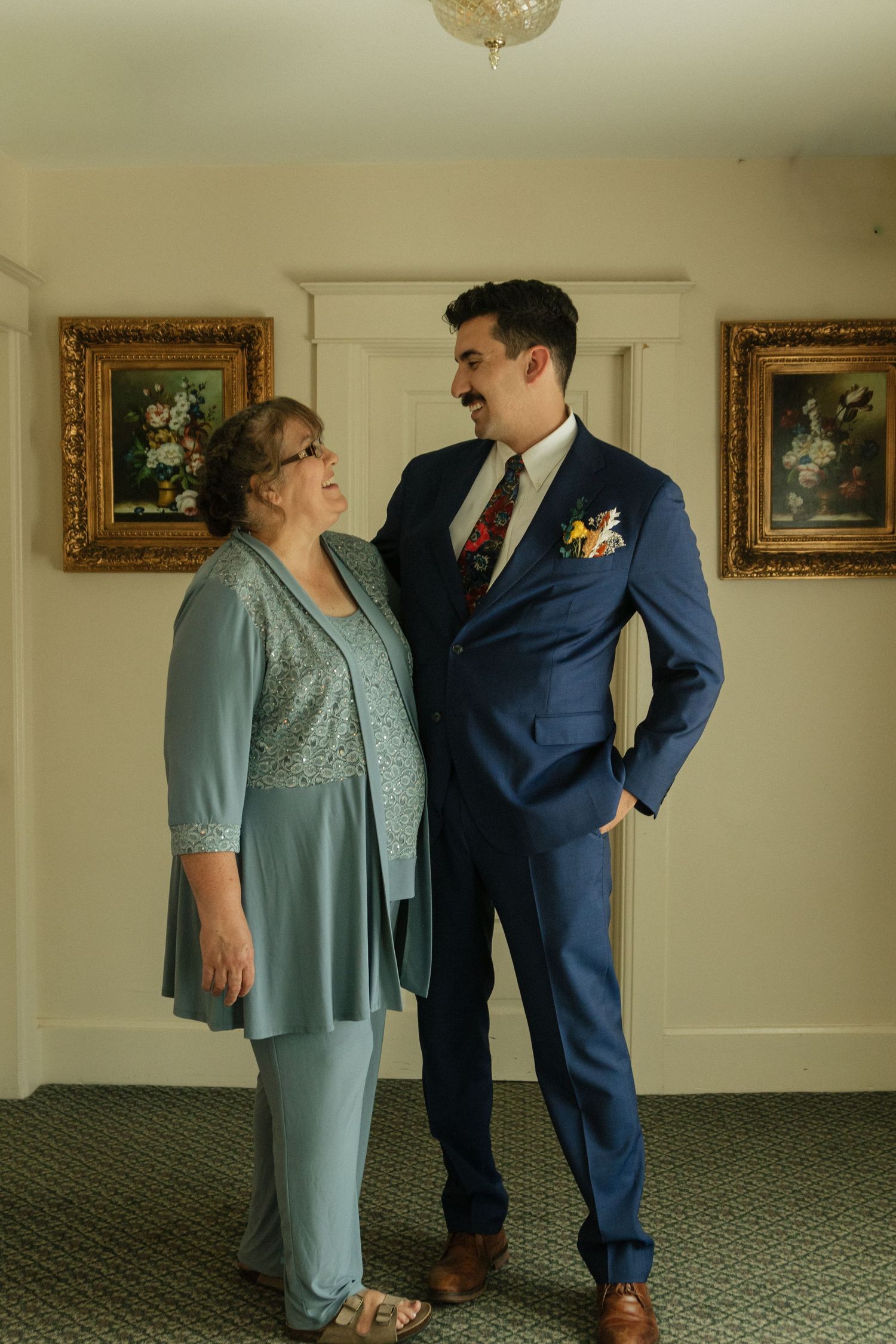 People in formal attire pose while standing in an elegant room with framed artwork on the walls.