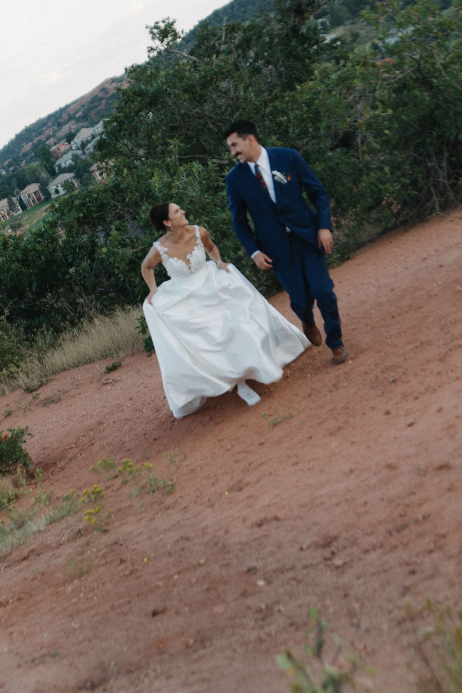 A wedding couple walking along a scenic mountain trail during sunset.