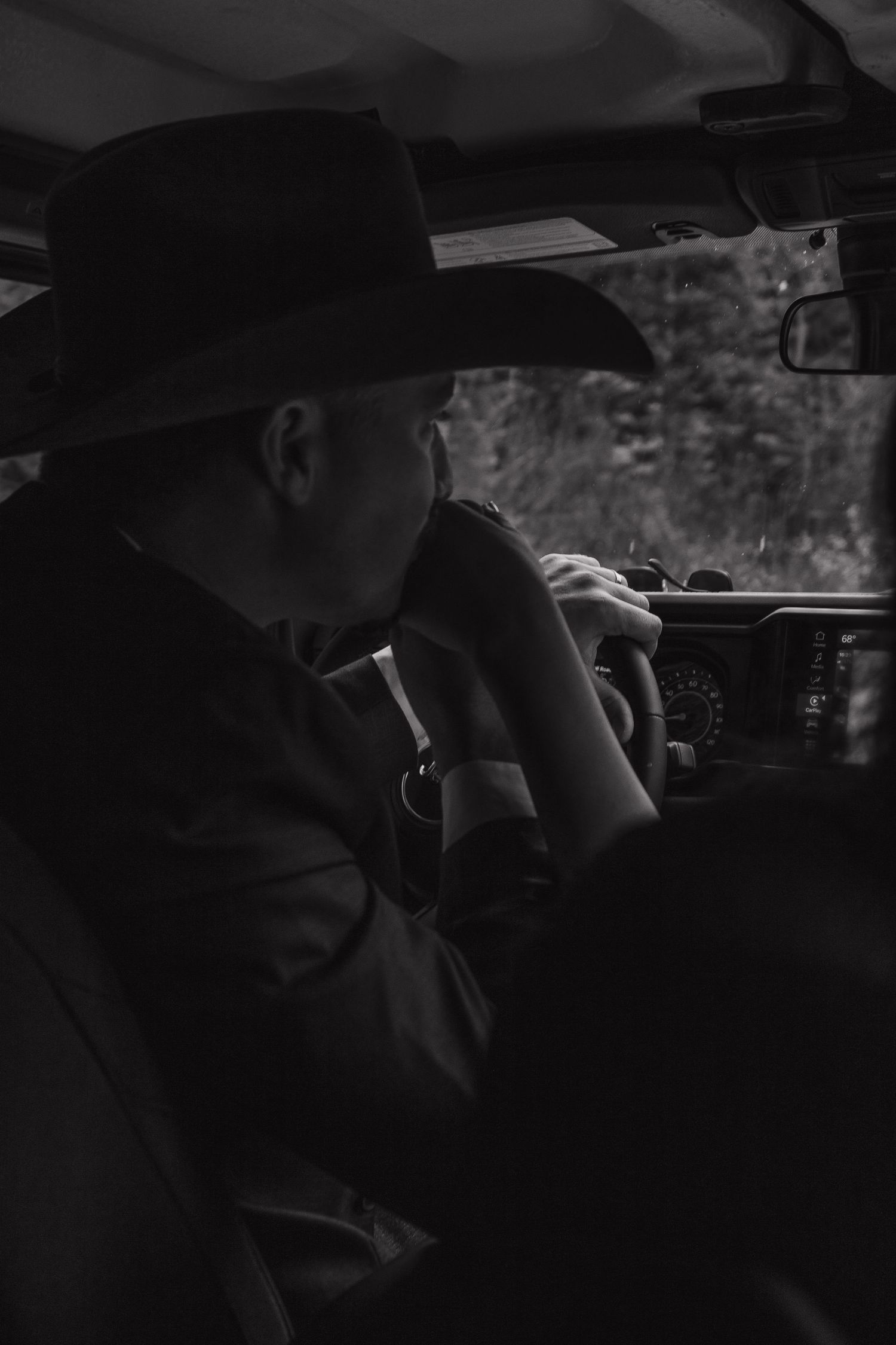 A silhouetted figure in a cowboy hat sits in the driver's seat of a vehicle.