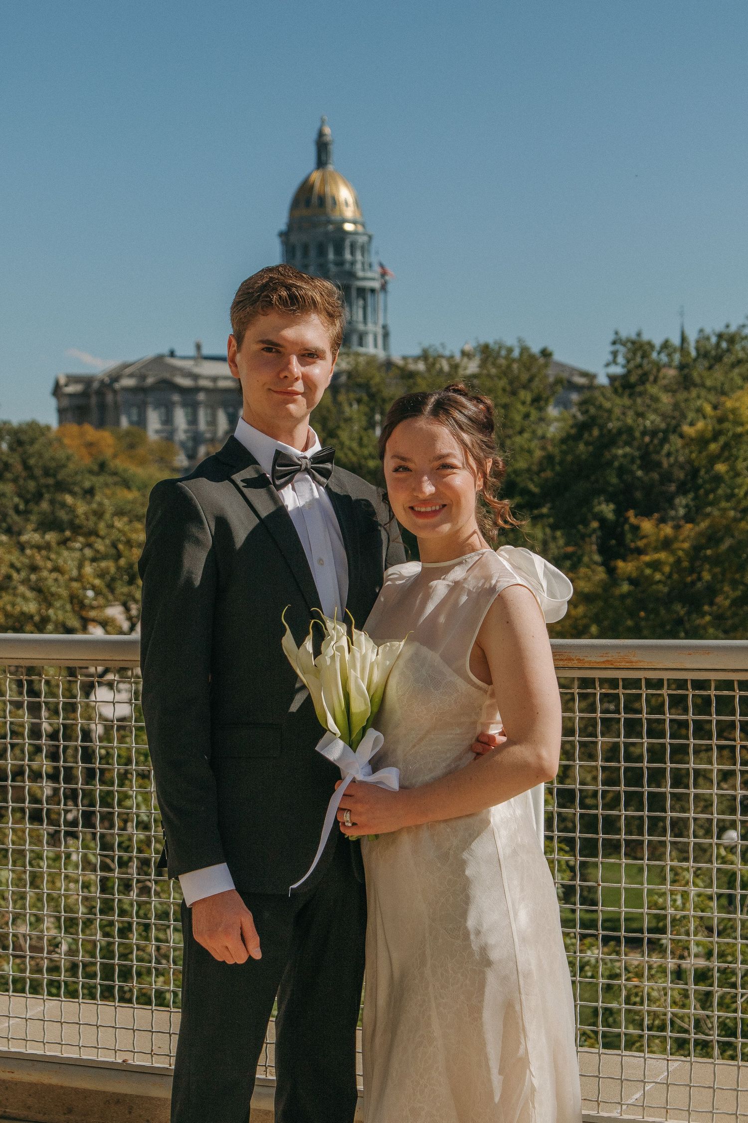 Wedding couple posing outdoors with golden dome building visible in background.