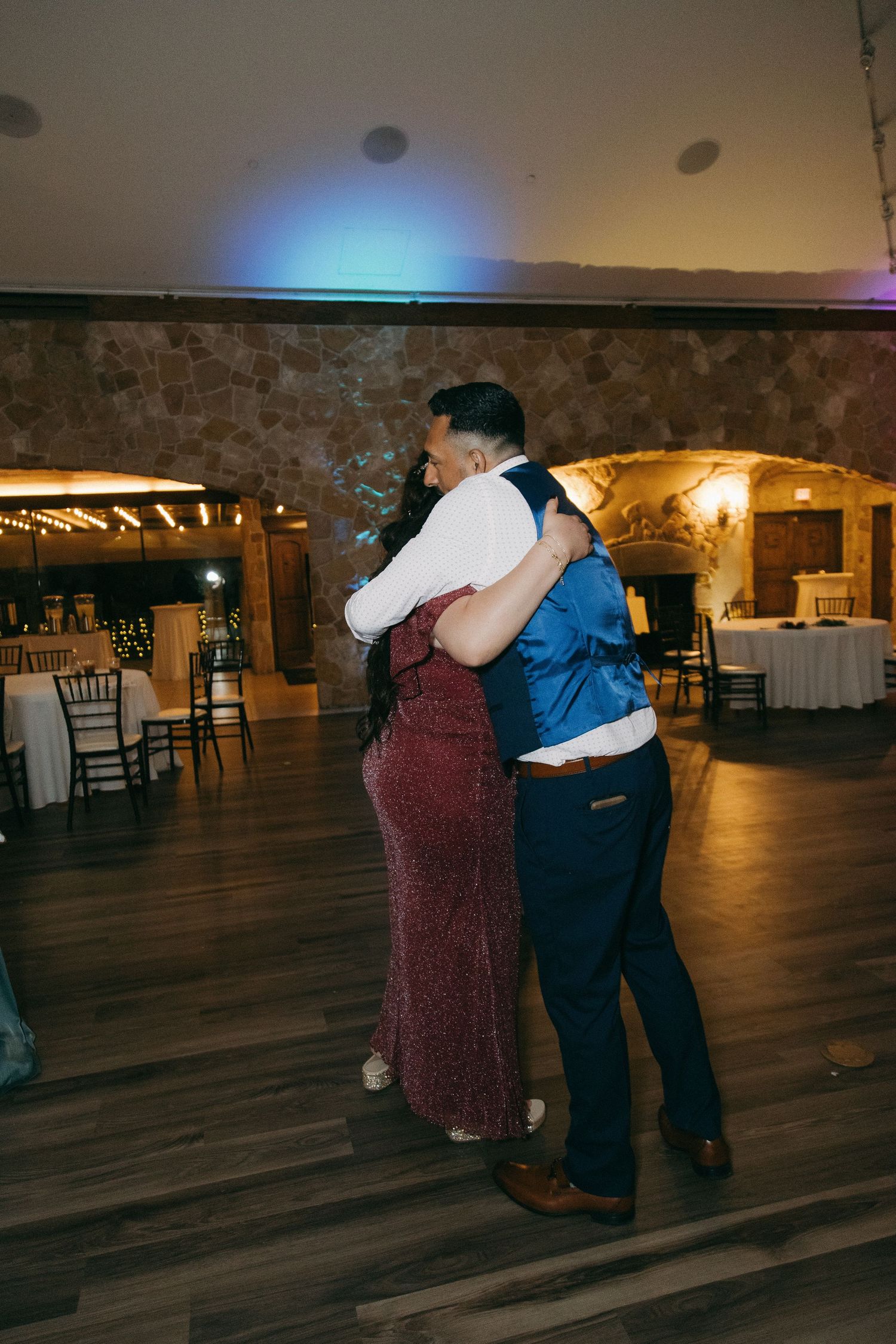 Couple shares slow dance embrace on wooden dance floor at romantic wedding reception venue.