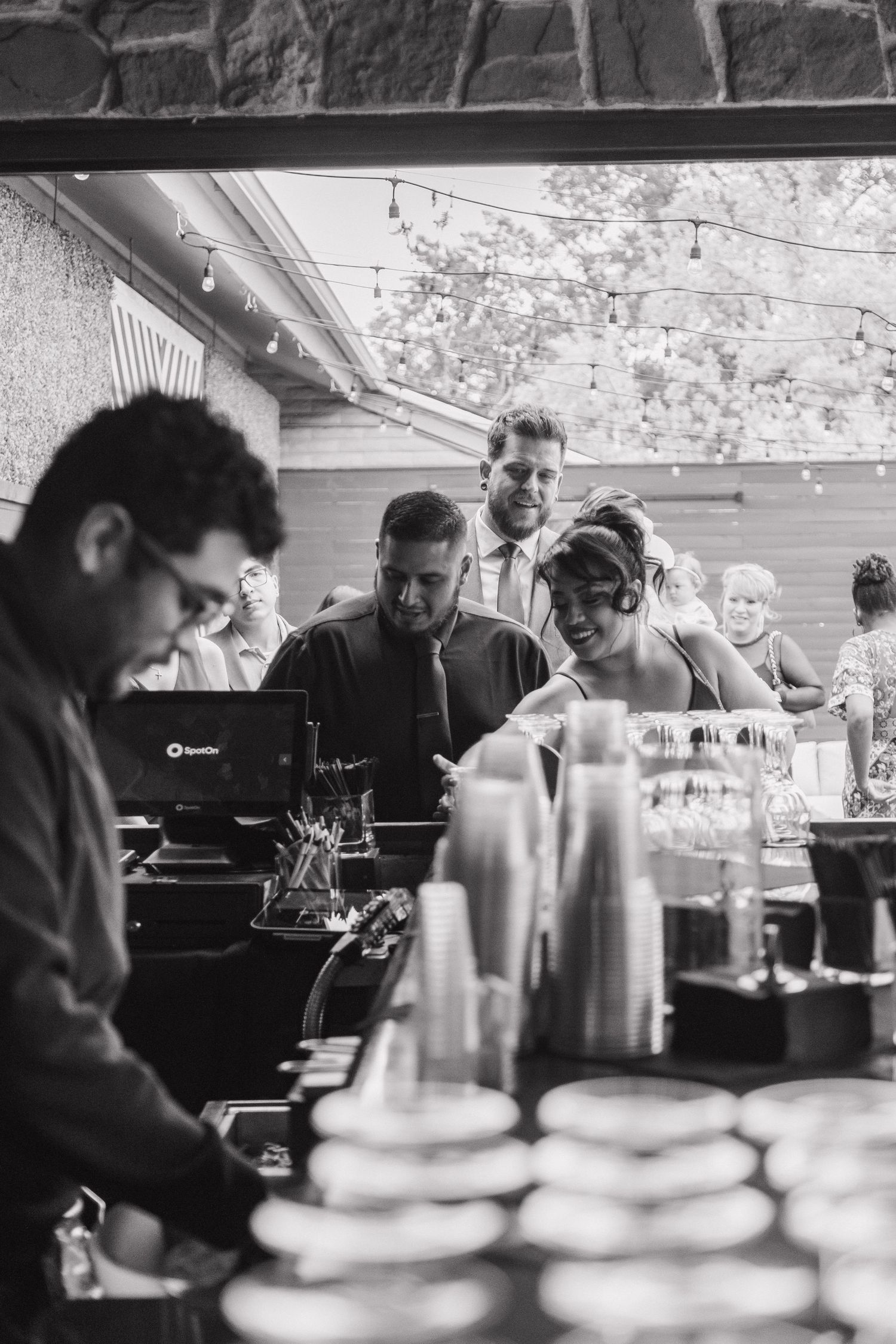 Black and white photo of wedding guests gathered at an outdoor bar during a wedding reception.