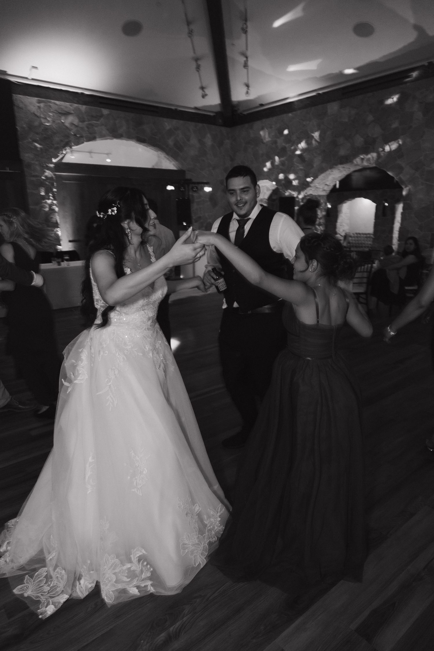 Black and white photo of bride, groom, and bridesmaid dancing together at wedding reception.