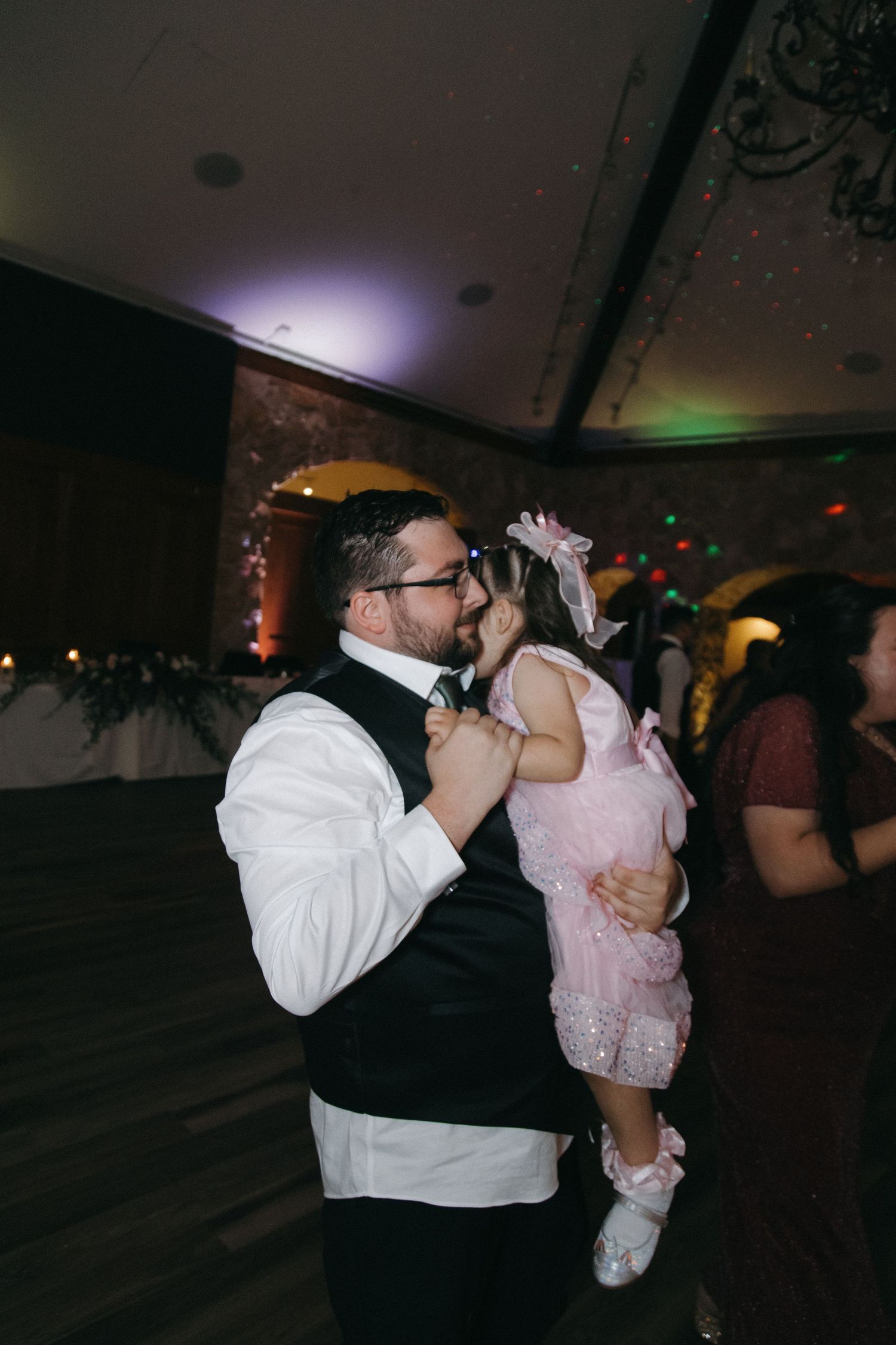 Father tenderly holds young girl in pink dress while dancing at wedding reception celebration.