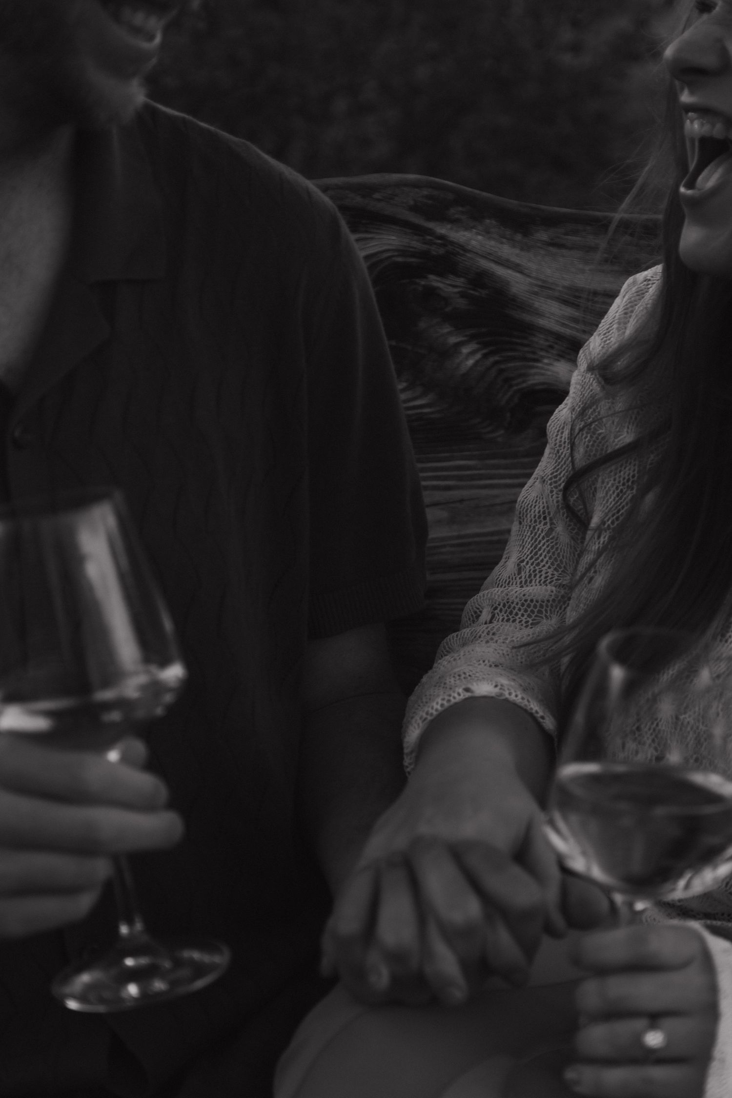 Black and white photo of couple holding hands and wine glasses together.