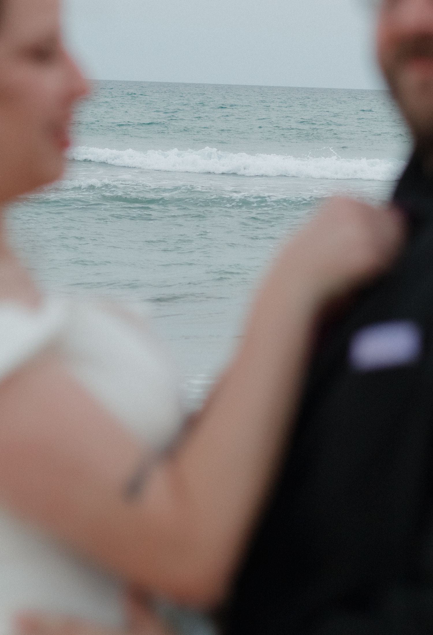 Blurred couple in wedding attire on a beach with ocean waves in the background.