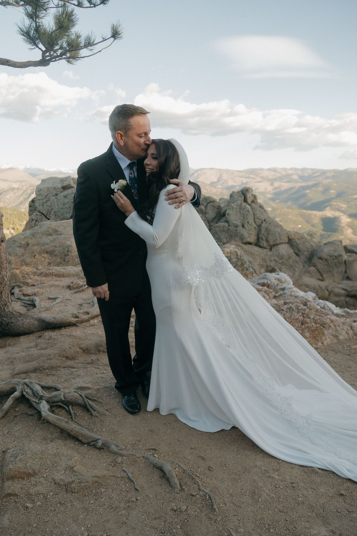 Bride and groom share romantic kiss on rocky mountain summit with sweeping Colorado landscape behind them.