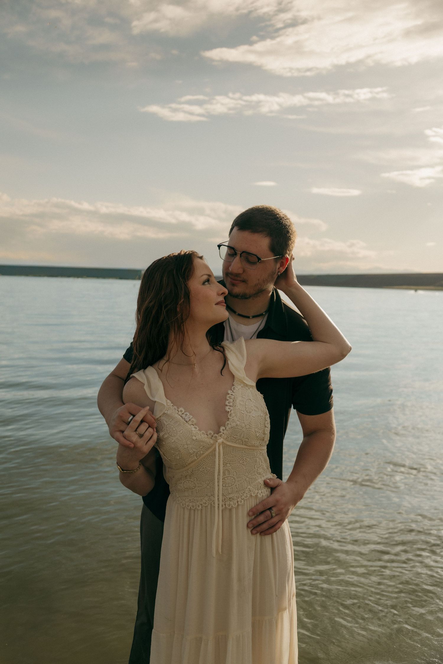 Couple embracing tenderly on a lakeside beach during a warm sunset evening.