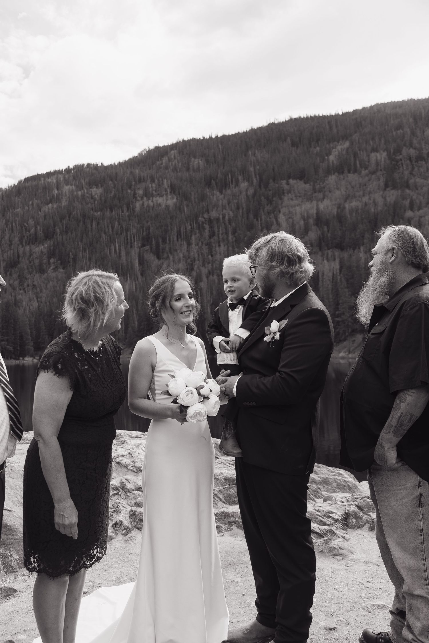 Bride and groom share a moment with family at mountain lakeside wedding.