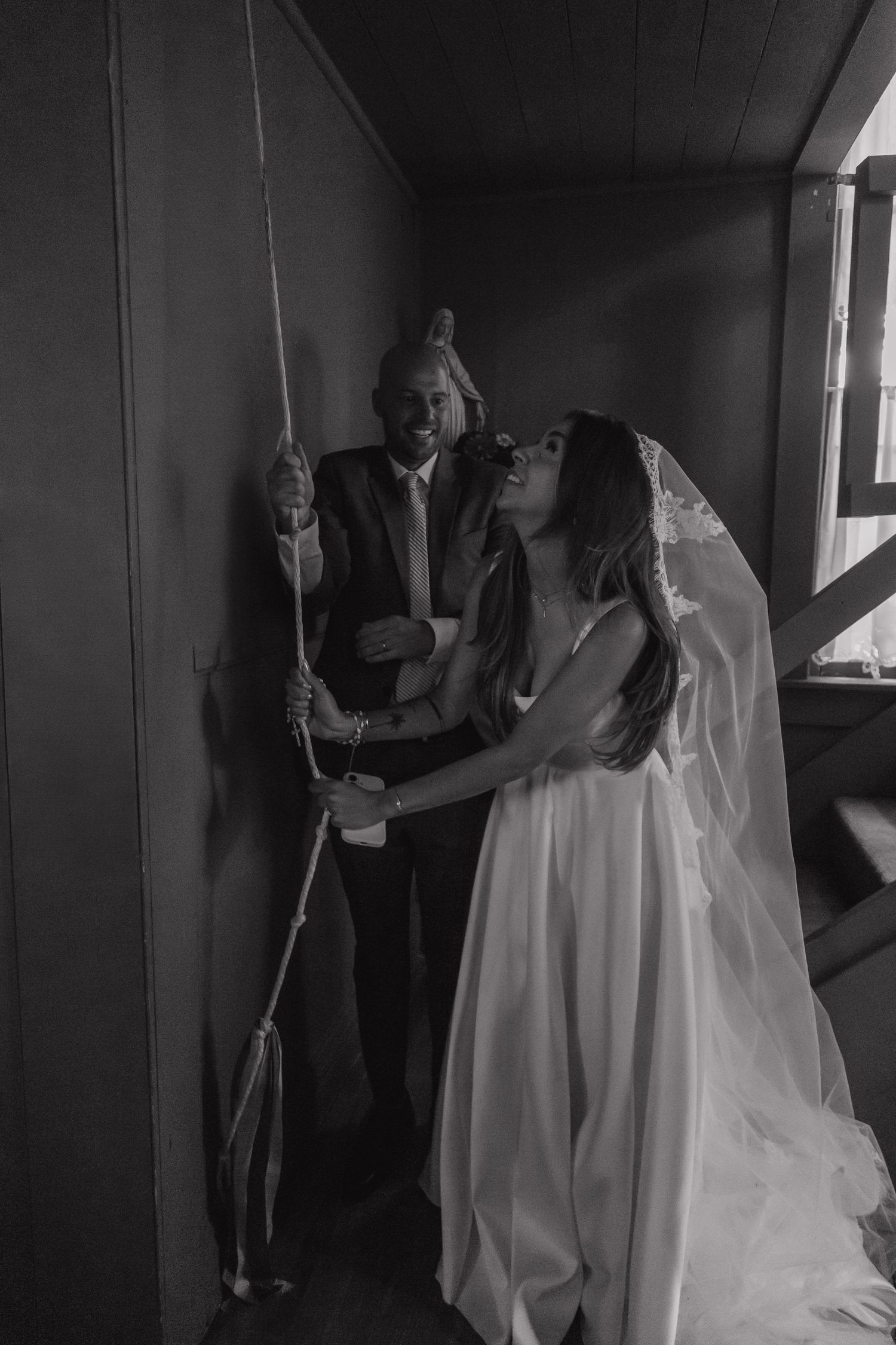 Black and white photo of bride and groom ringing a church bell together on their wedding day.