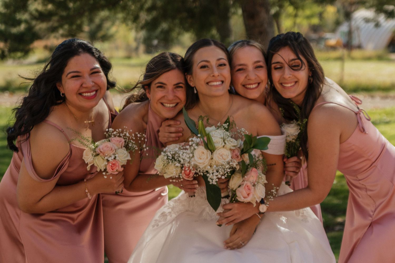 A group of bridesmaids in pink dresses share joyful moments together at an outdoor wedding celebration.