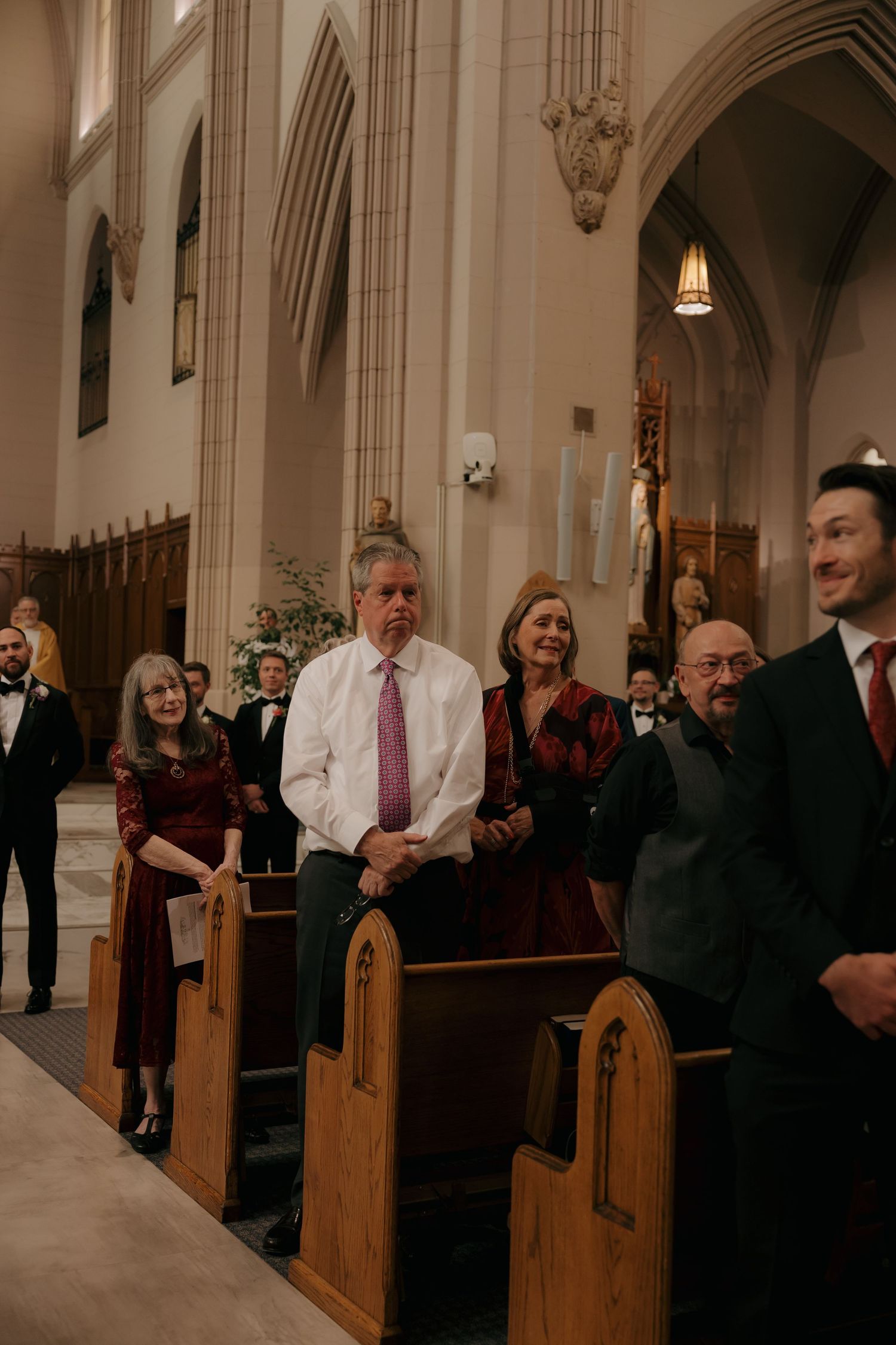 Wedding guests standing in church pews during a ceremony in a Gothic-style church.