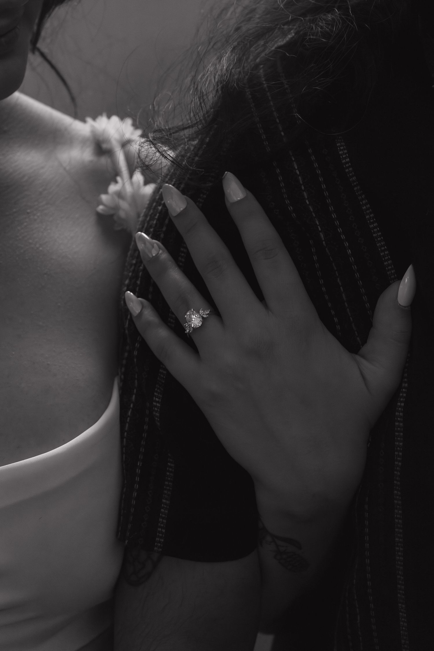 Close-up black and white photo showing hands with an engagement ring against a white dress.