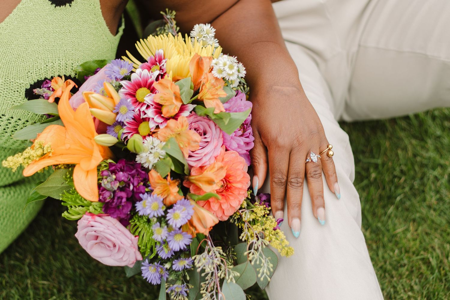 Close-up of vibrant wedding bouquet with orange lilies, purple carnations and pink roses next to white dress.
