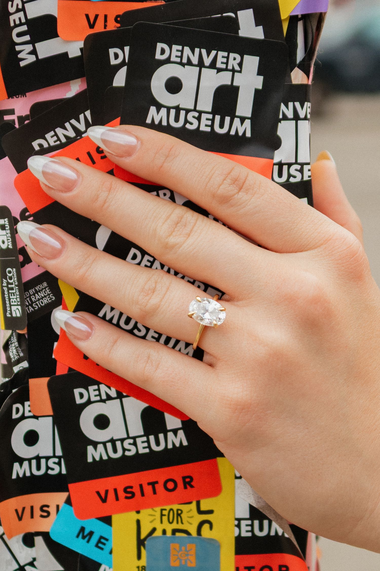 Manicured hands holding colorful Denver Art Museum visitor passes and tickets.