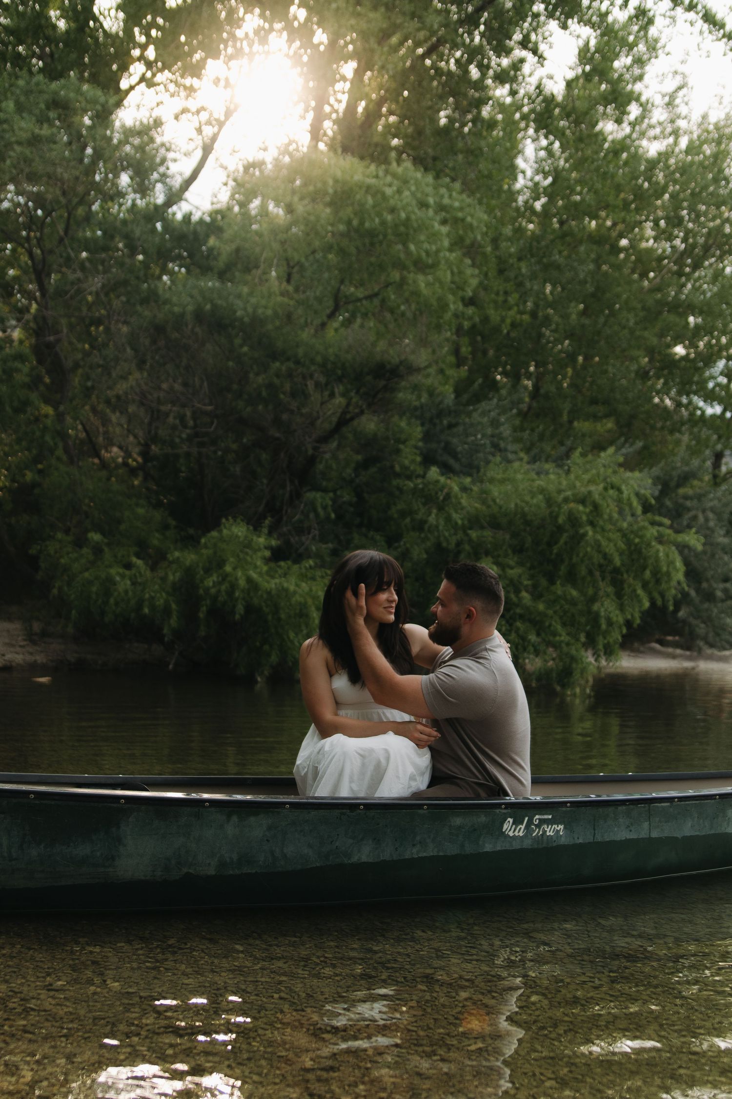 Couple embracing in a canoe on calm waters with lush greenery in the background.