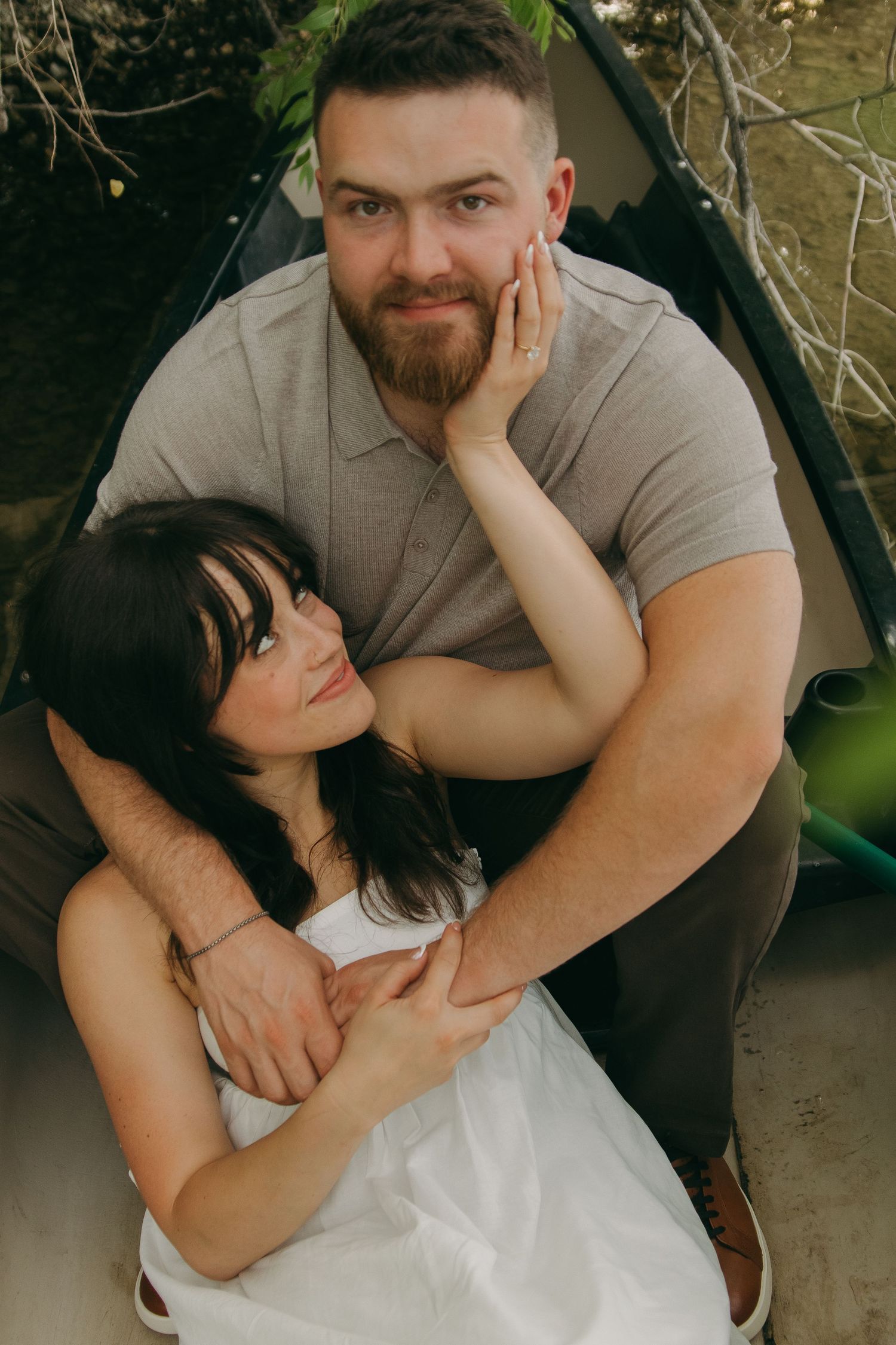A couple cuddles while seated together outdoors during a romantic photoshoot.