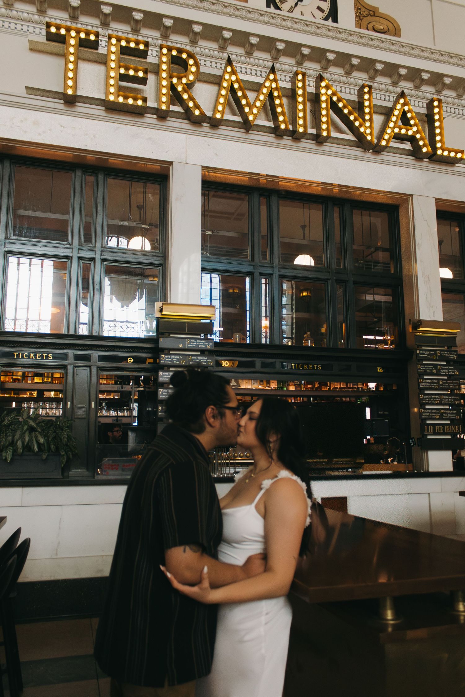 A romantic moment captured in front of an illuminated Terminal sign at a historic train station interior.