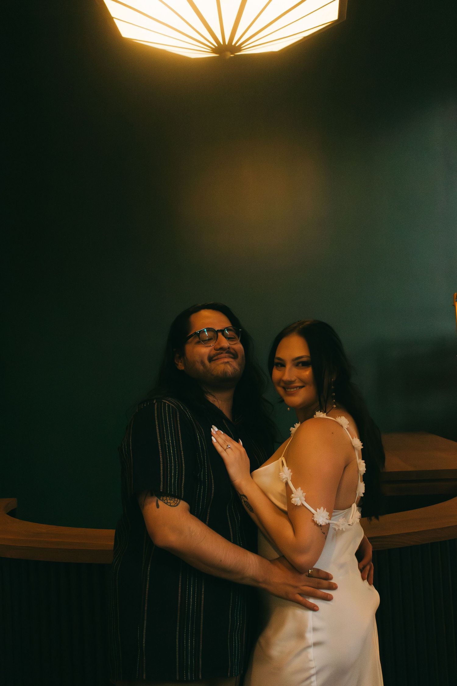 A couple embraces under a striking geometric ceiling light fixture in a moody atmospheric setting.