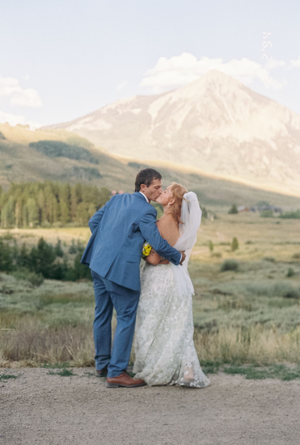 Bride and groom share a kiss with a dramatic snow-capped mountain peak glowing at golden hour.