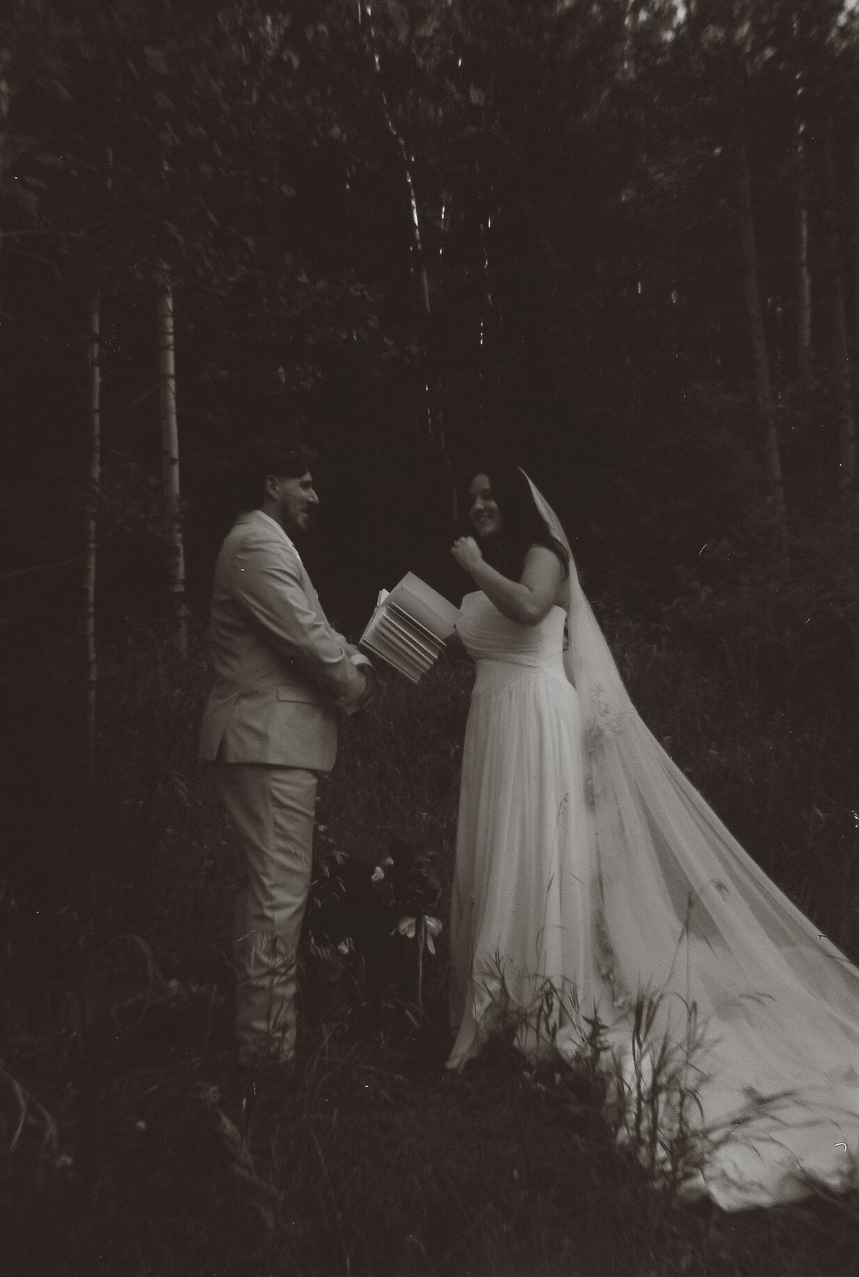 Black and white photo of bride and groom exchanging vows in a dark forest during an intimate outdoor elopement ceremony.