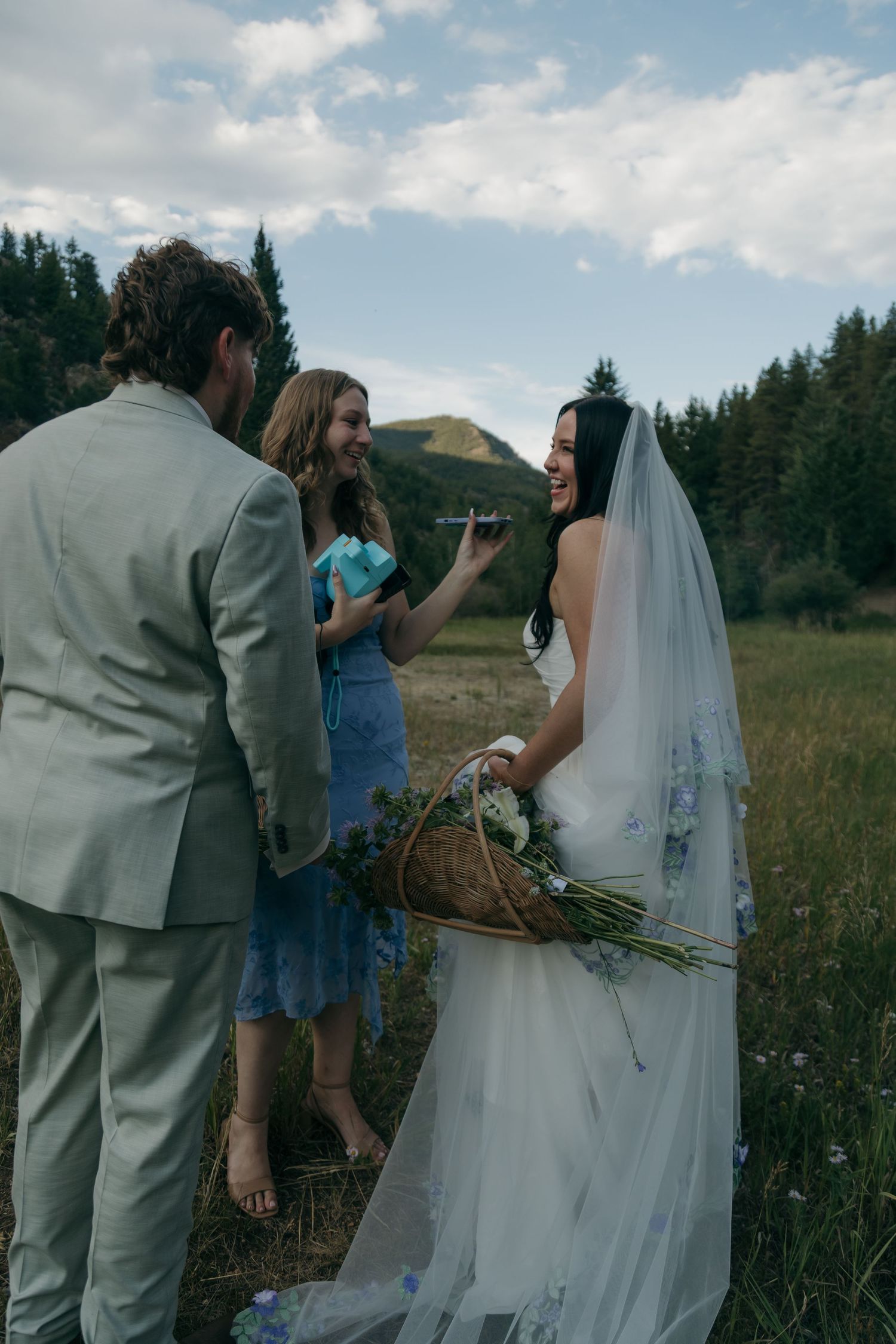 Bride laughs joyfully with officiant in mountain meadow during outdoor wedding ceremony.