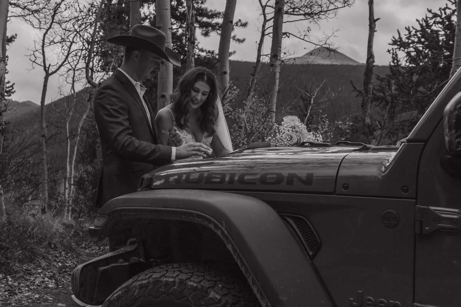 A couple posing near a classic car with mountain scenery in the background.