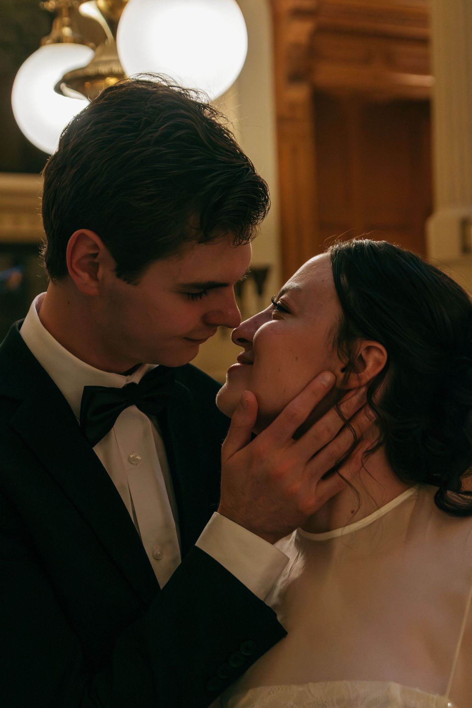 Intimate wedding couple sharing a tender moment in warm indoor lighting.
