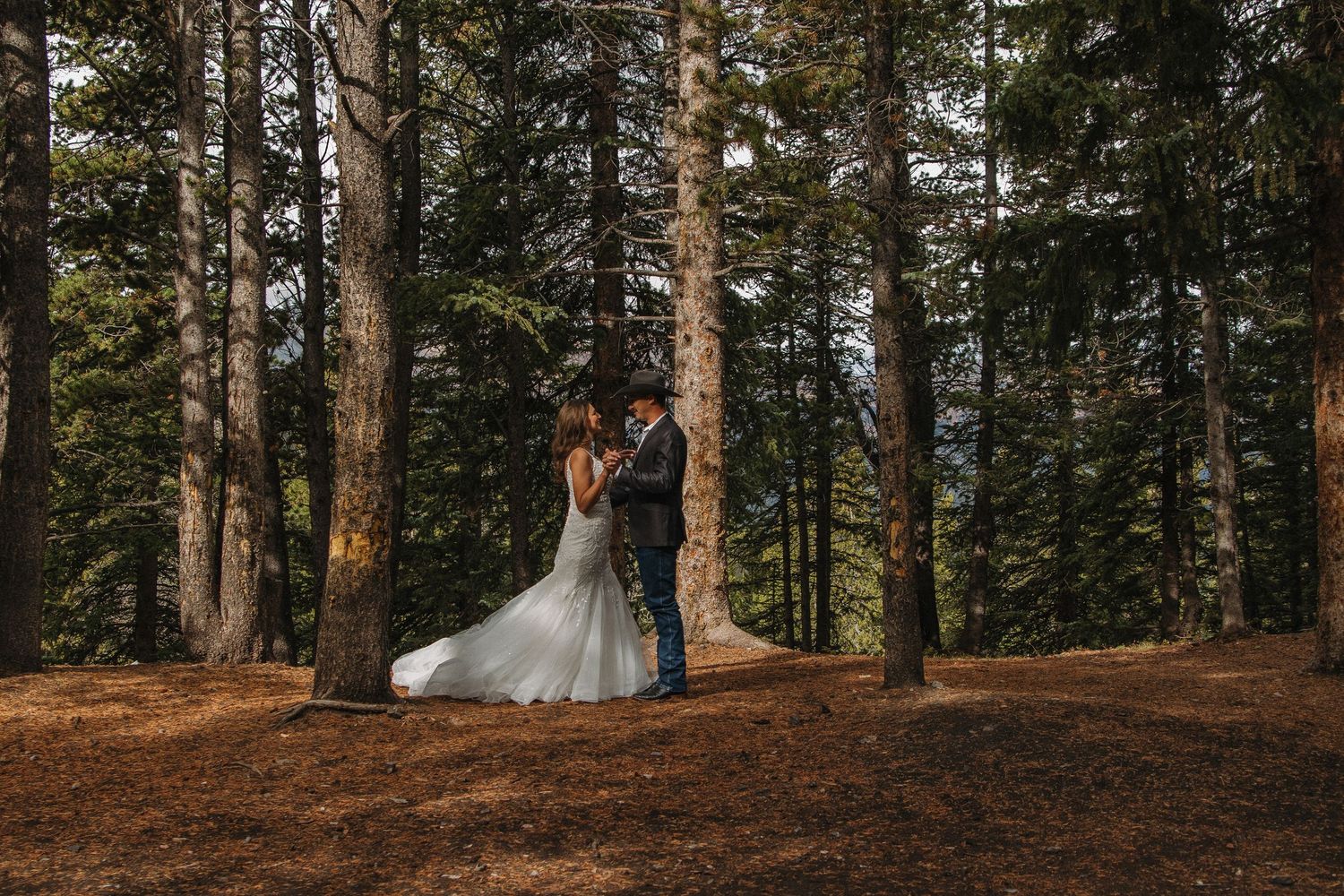 A romantic forest wedding scene with a couple surrounded by tall evergreen trees in a natural woodland setting.