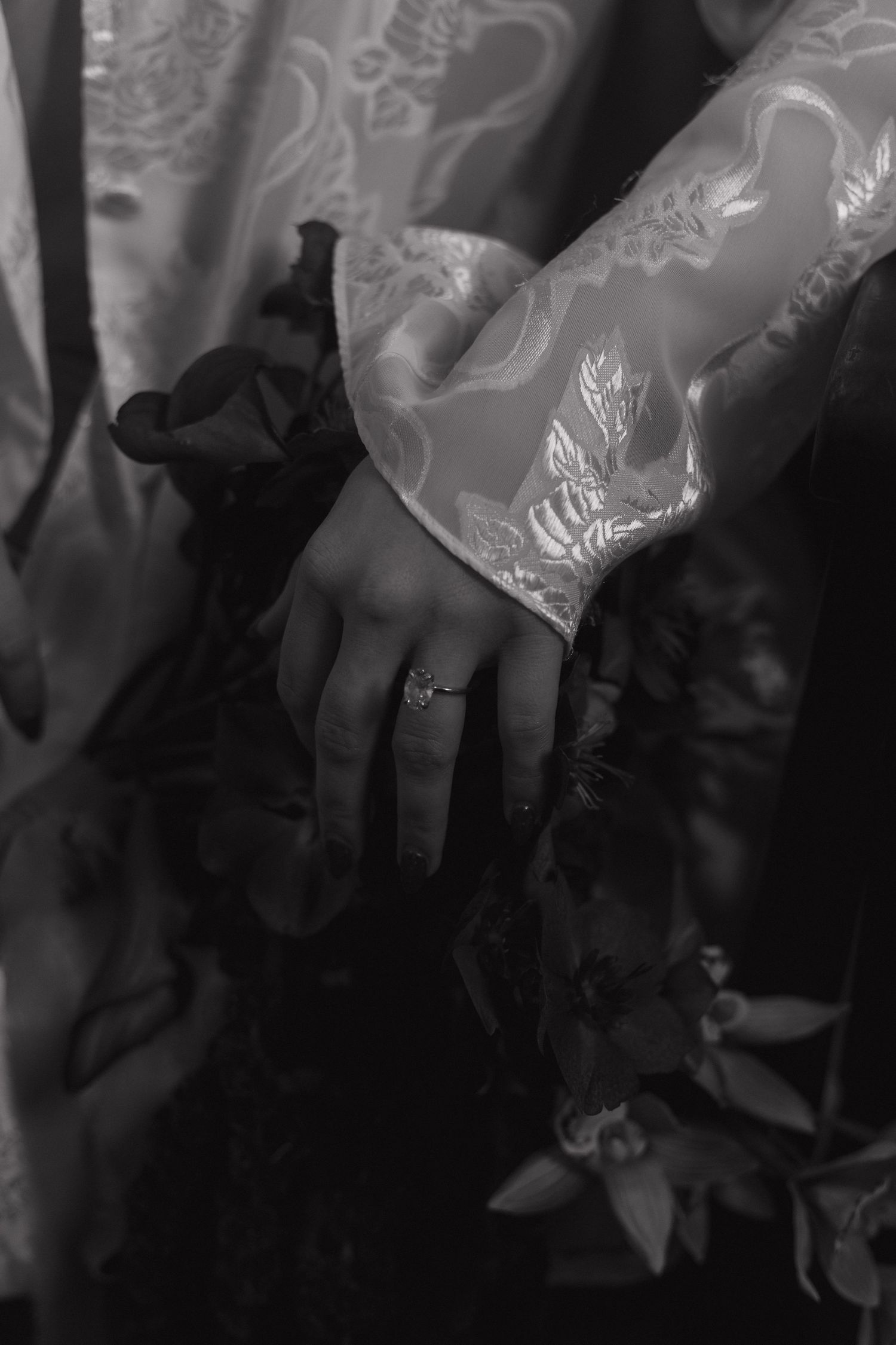 Close-up black and white photo of a hand wearing a ring with delicate lace sleeve detail.