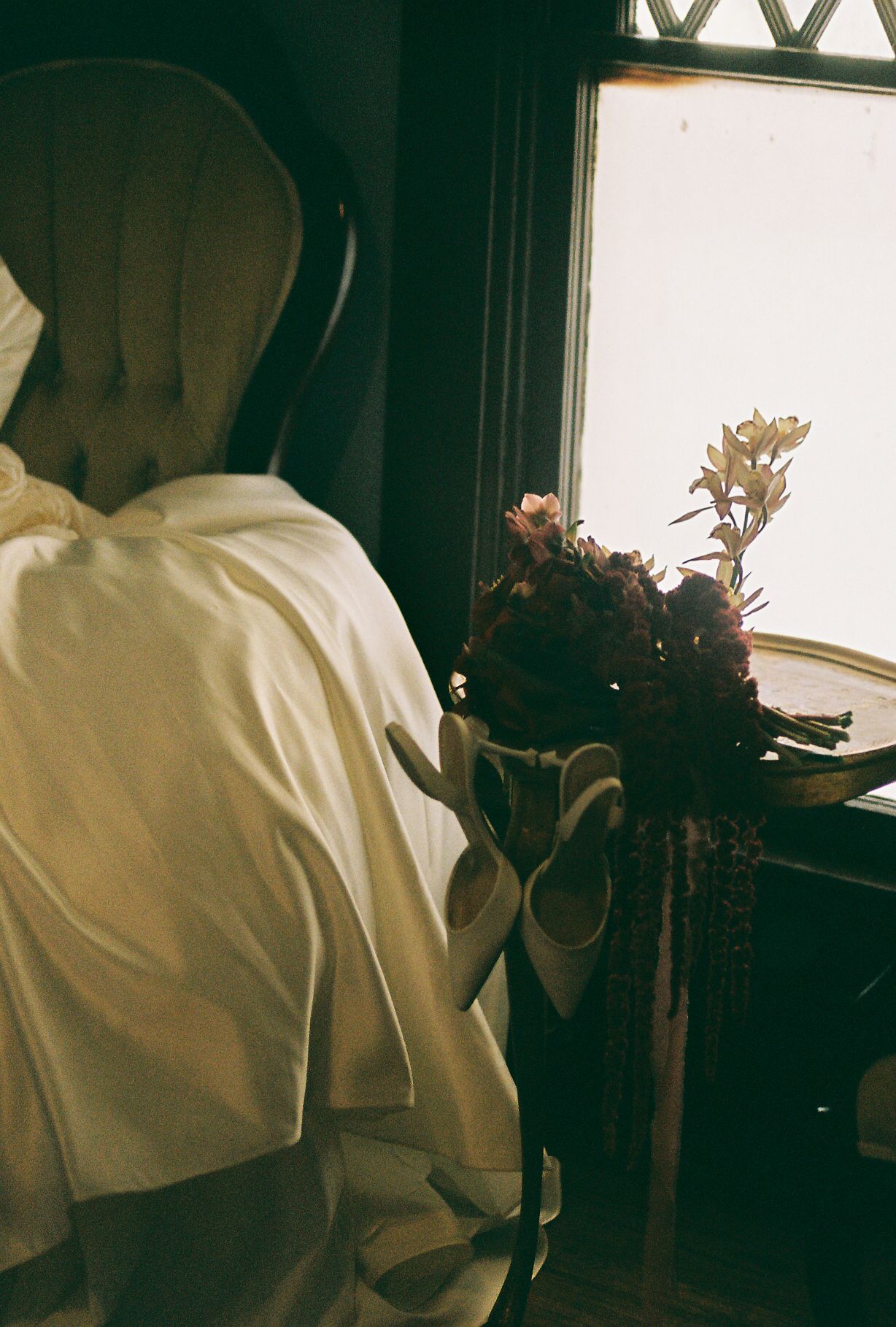A person in white holds a dark floral bouquet near a window with diamond-patterned glass.