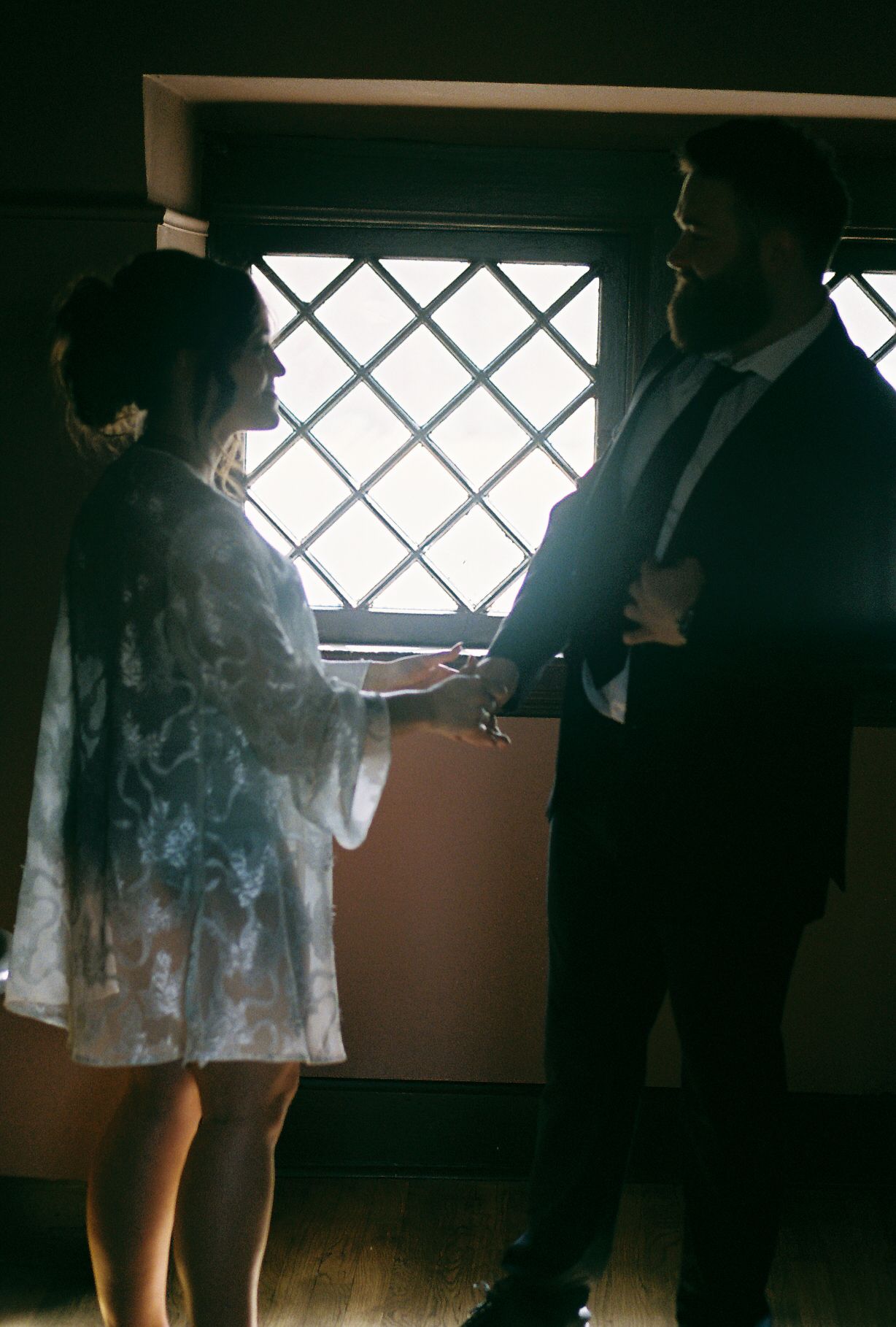 A couple stands by a latticed window in intimate conversation.