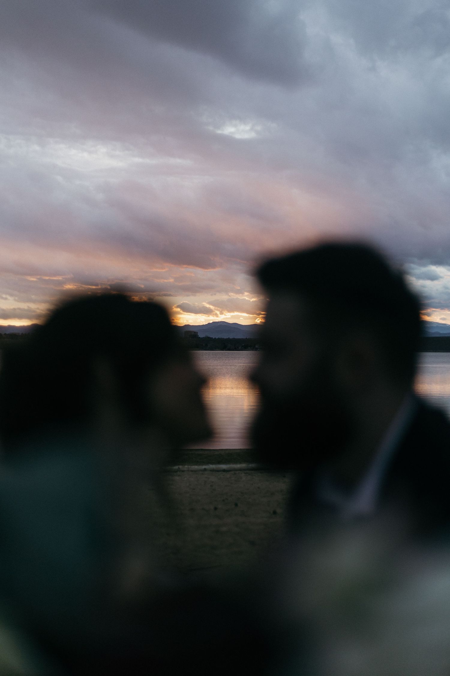 Silhouettes of figures against a dramatic sunset sky over water with pink and orange clouds.