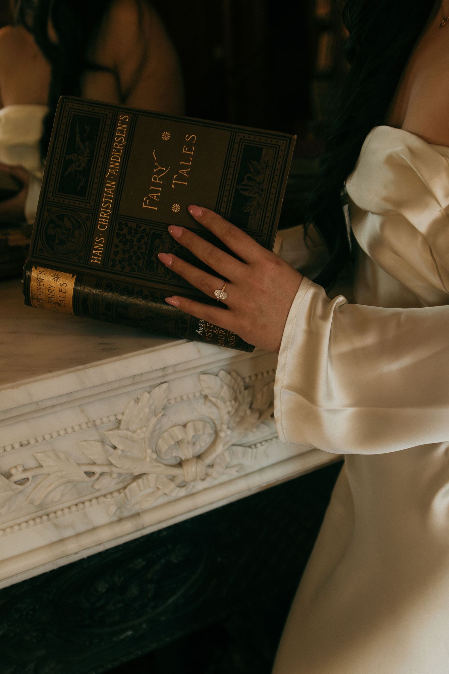 Close-up of hands holding an antique book against an ornate white marble surface.