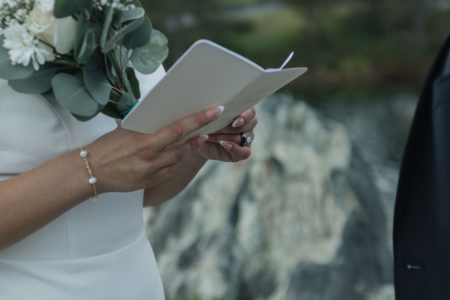 Close-up of hands holding wedding ceremony papers with eucalyptus bouquet visible.