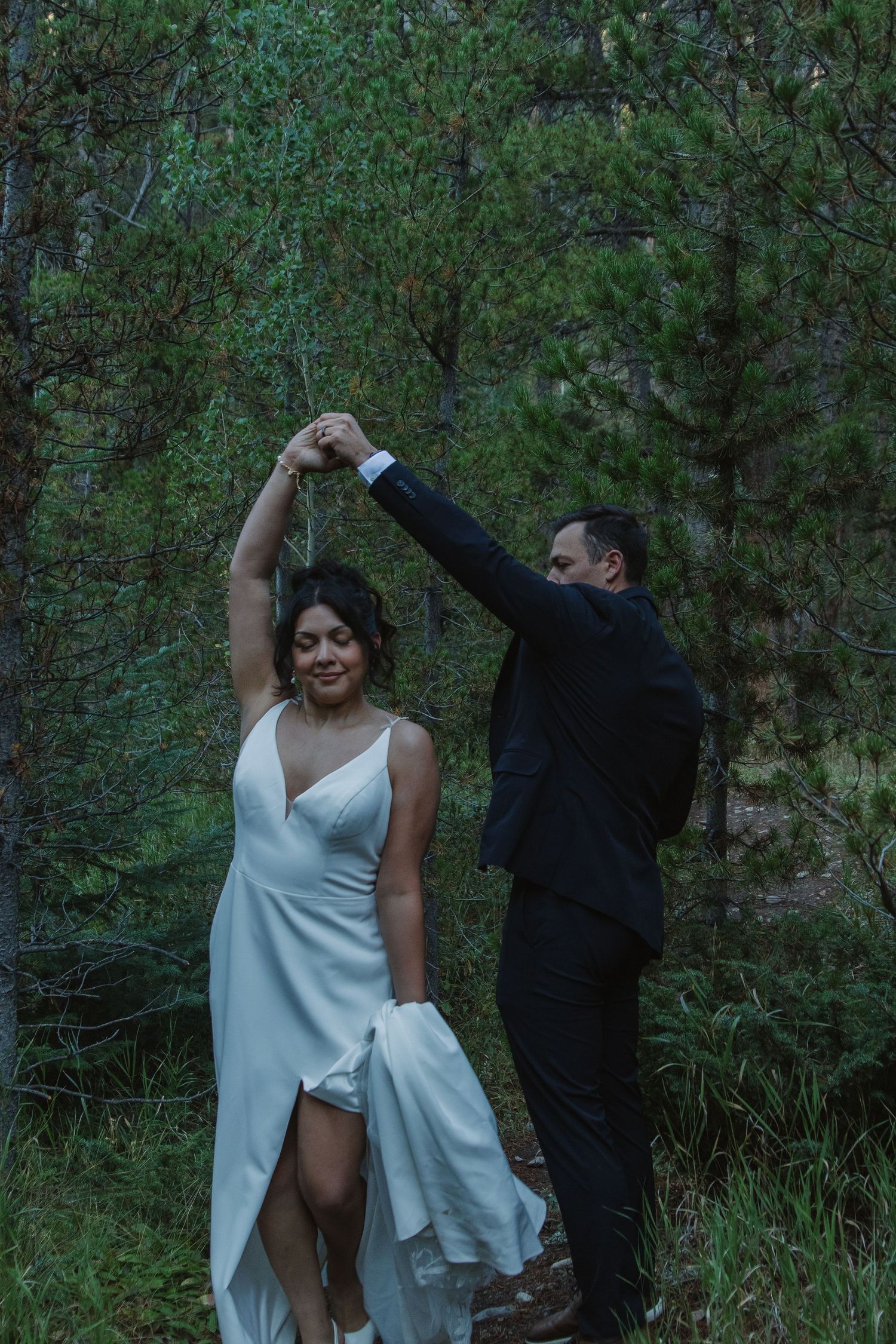 Dancing and twirling in formal attire by the waterfront with forest views.