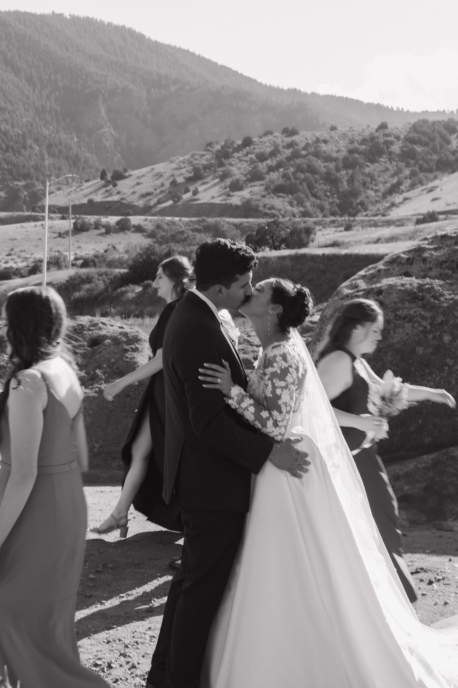 Black and white photo series of wedding party embracing outdoors with mountain views.