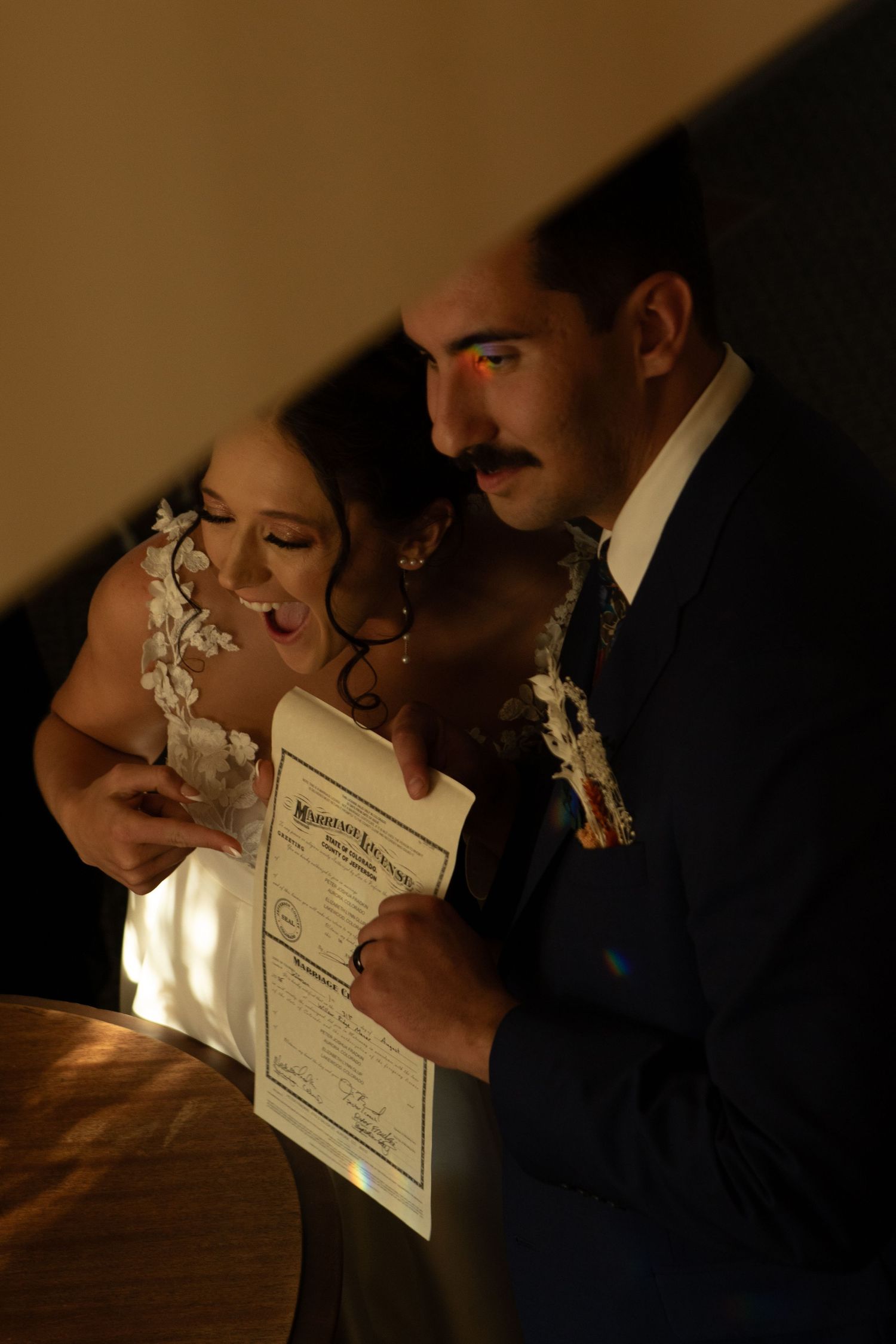 Artistic silhouette of couple kissing behind their marriage certificate in warm lighting.