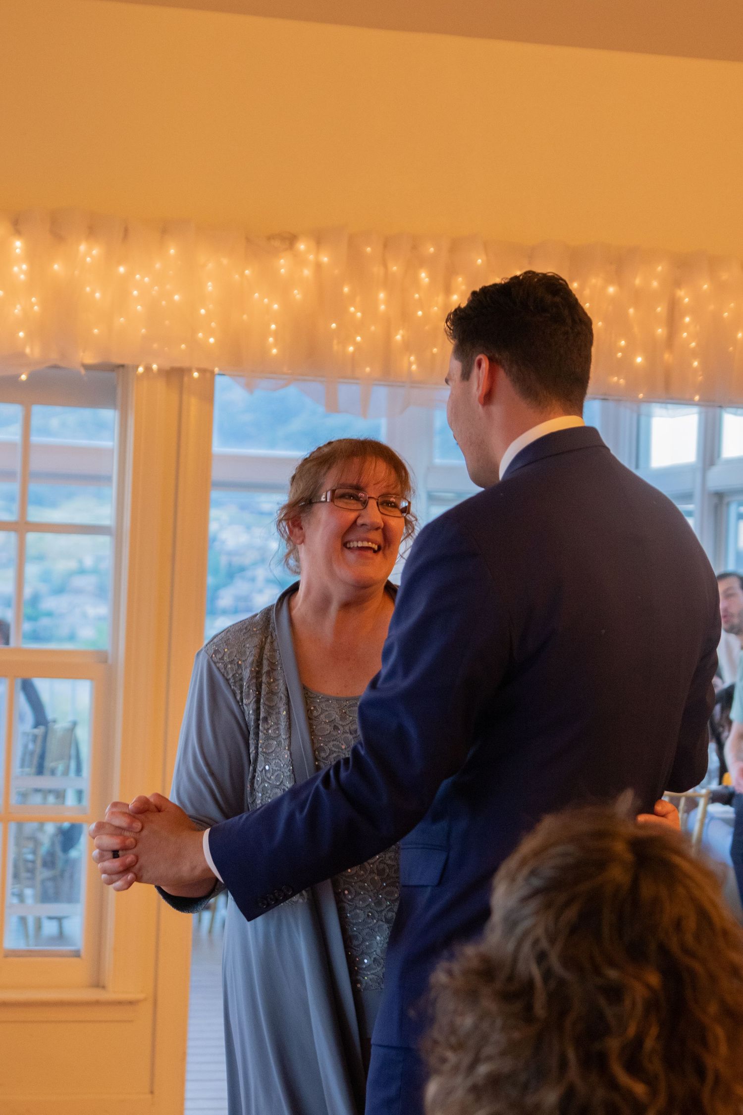Wedding reception guests share joyful moments in a warmly lit room with string lights.
