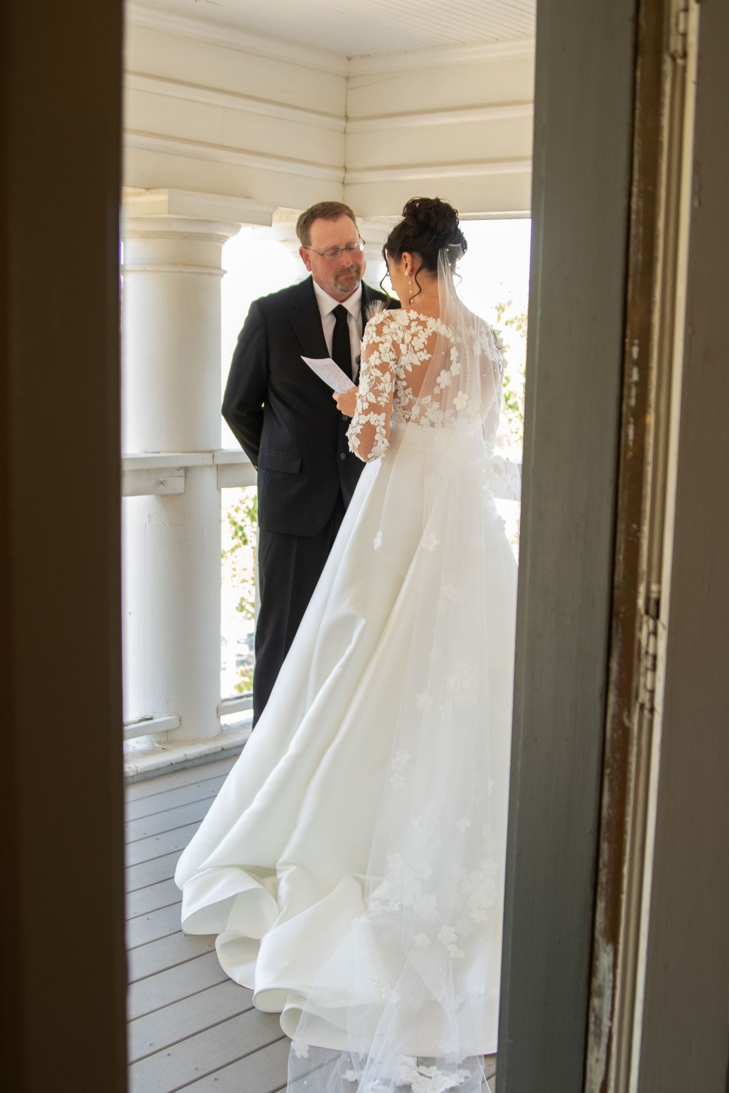 Wedding couple's first look captured through window reflections on porch.