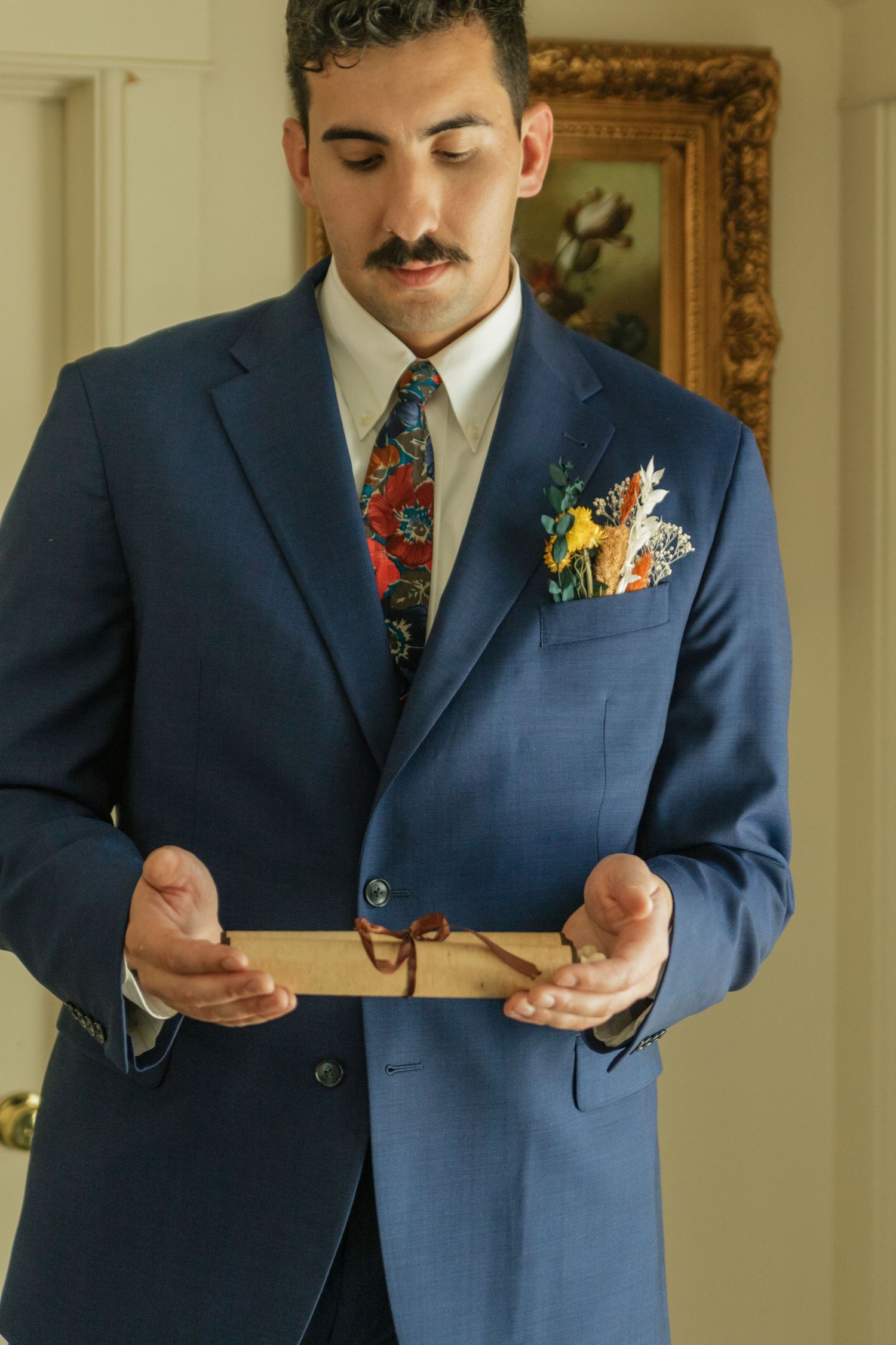 Groom in navy suit with floral boutonniere reading from a card.
