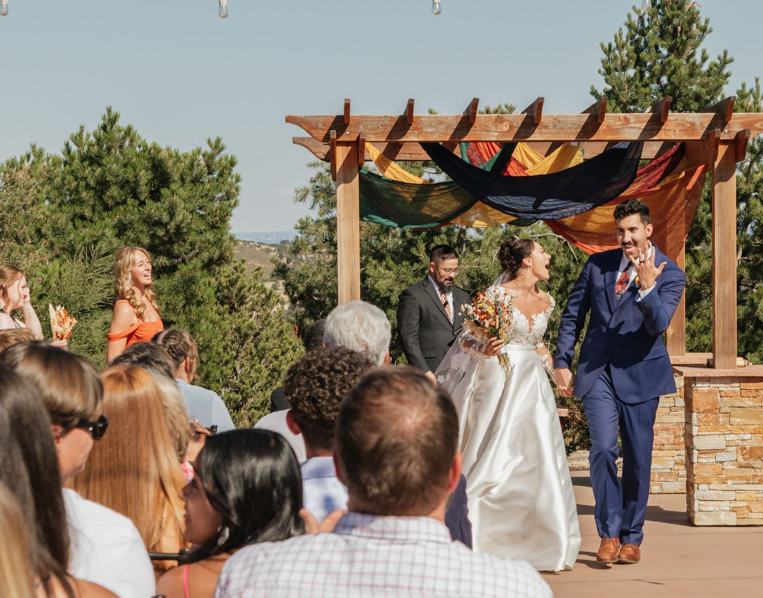 Wedding party gathered for outdoor ceremony under wooden pergola.