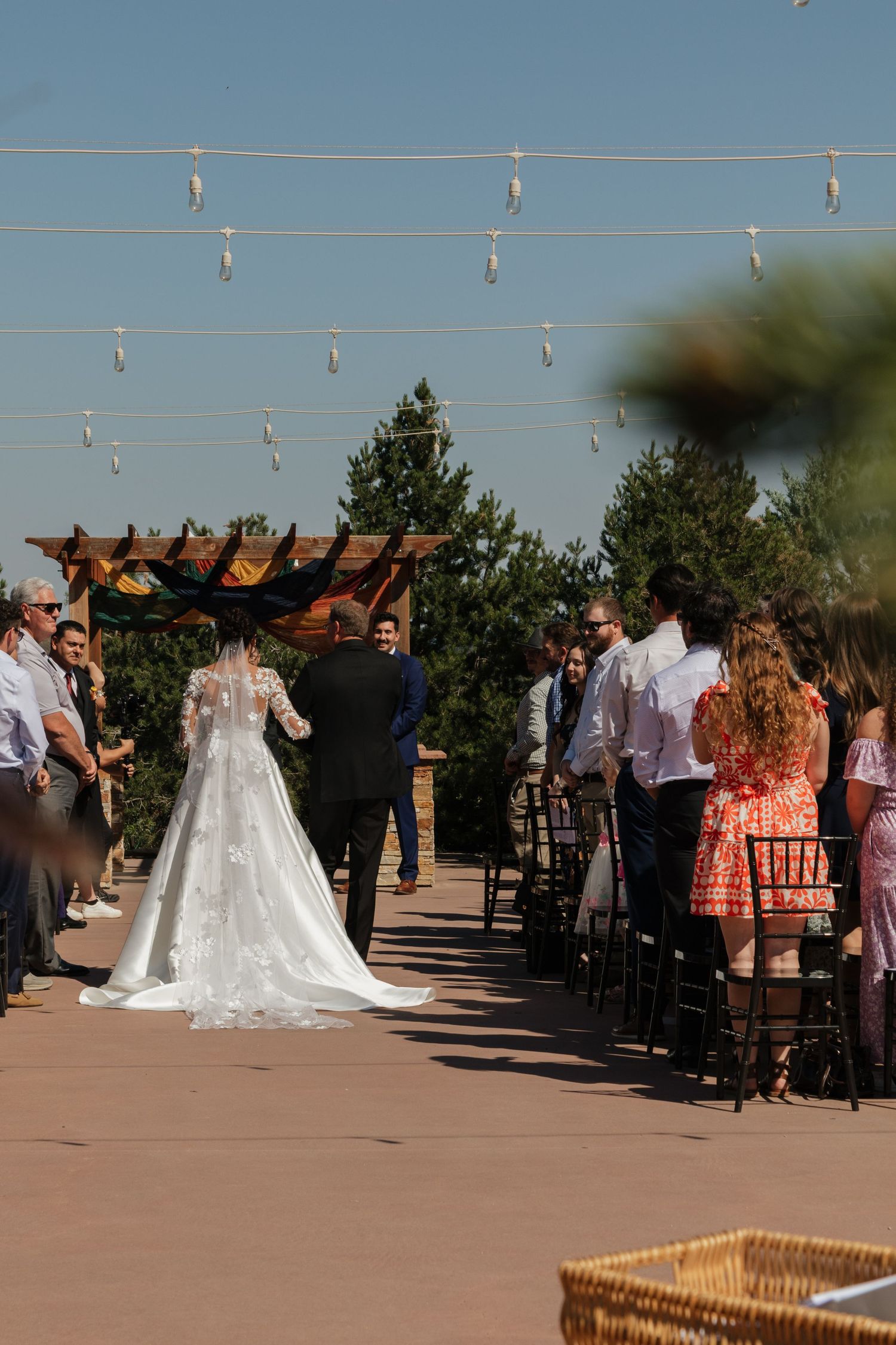 Outdoor wedding ceremony taking place under string lights with guests seated on either side.